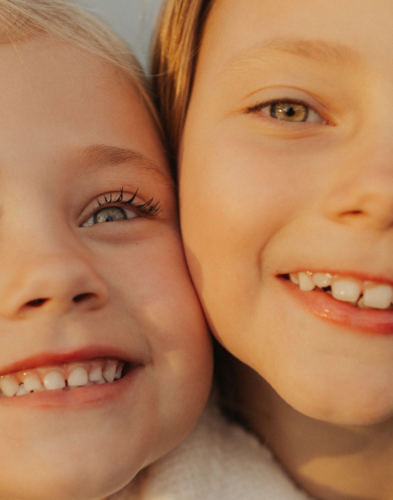 Close-up portrait of two smiling children with blue and green eyes cheek to cheek.