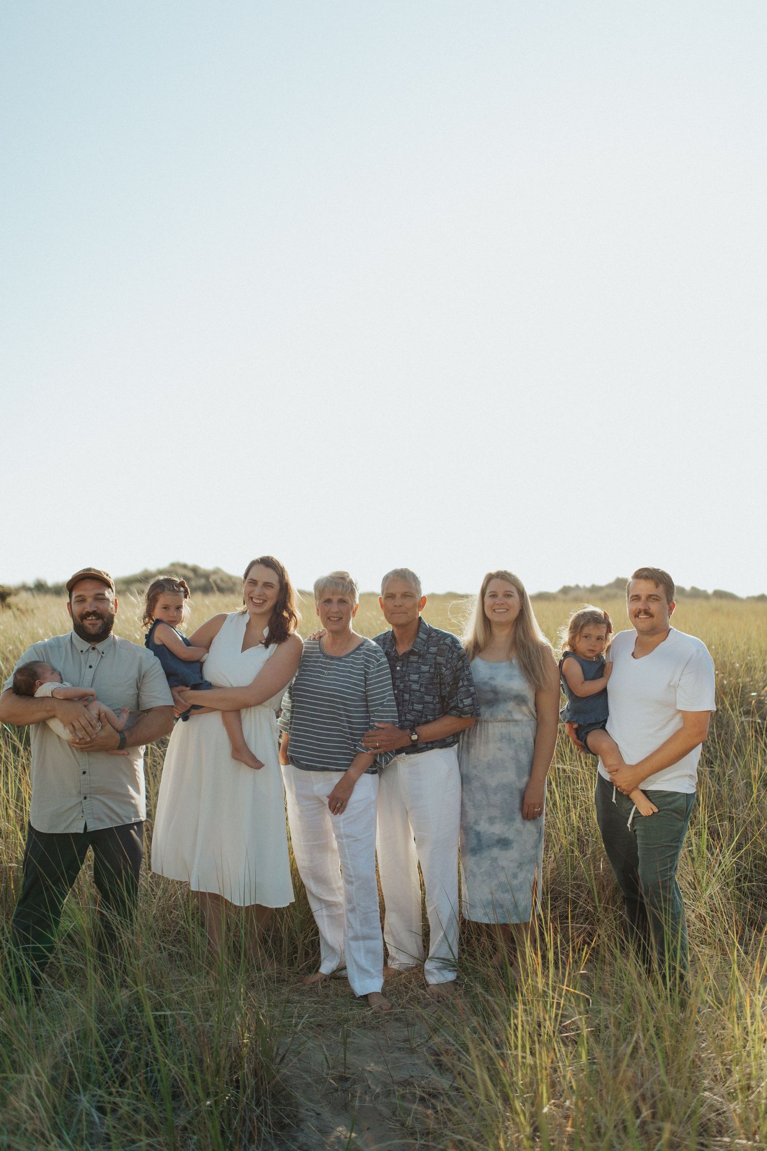 Extended multigenerational family portrait standing together in a golden grass field at sunset.