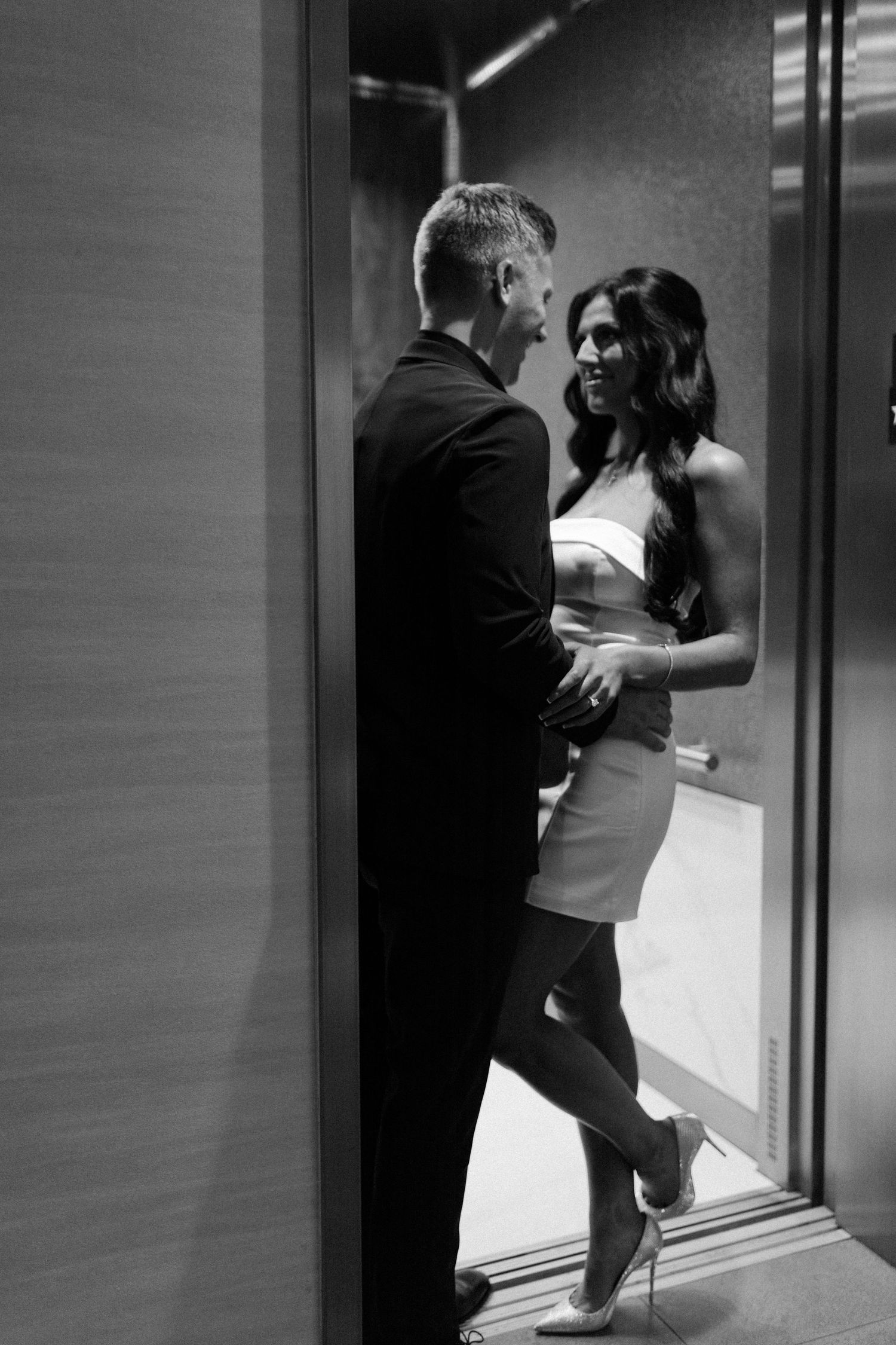 Black and white photo of couple sharing an intimate moment inside a sleek modern elevator.