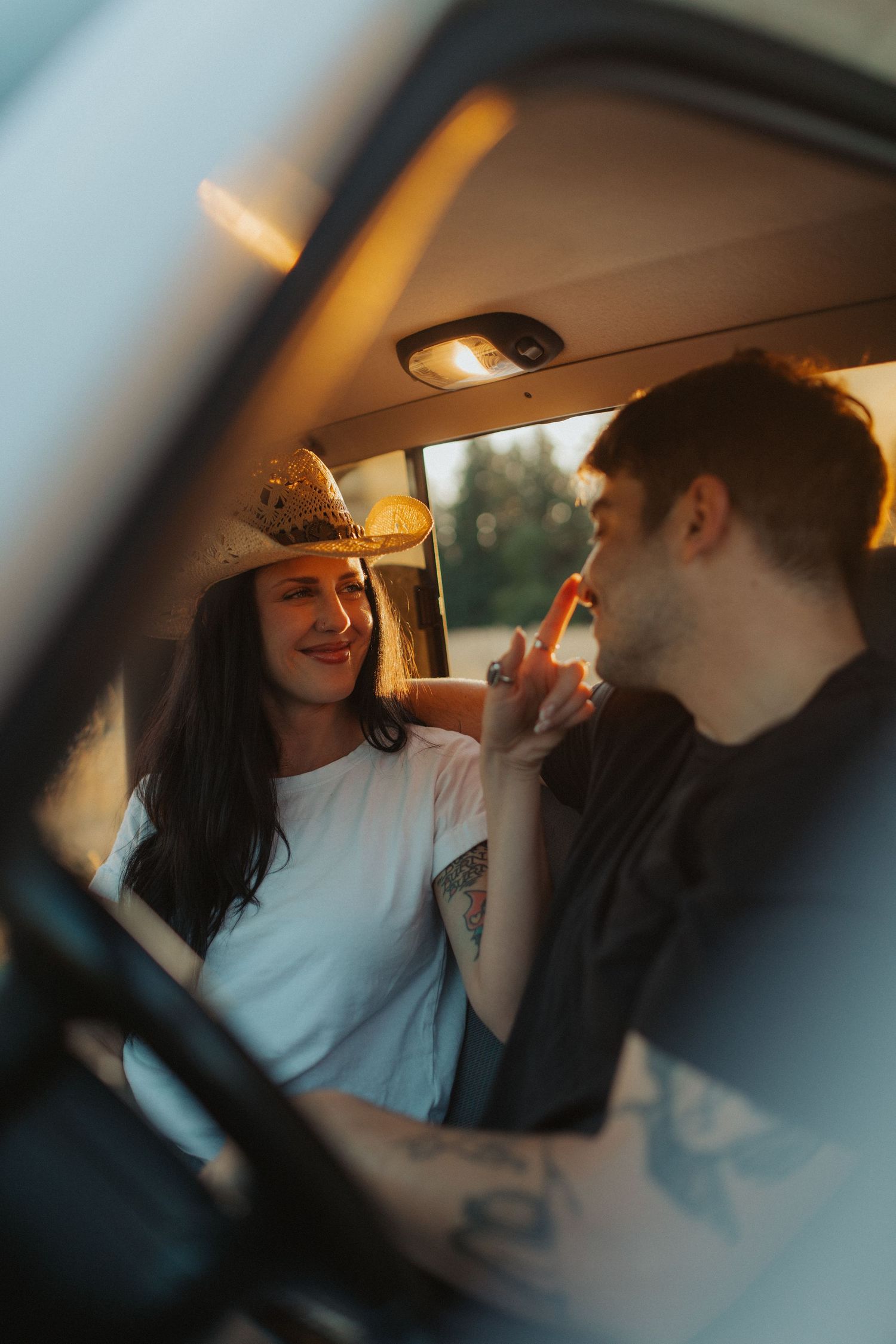 A smiling couple laughs and chats together inside a retro van at sunset.