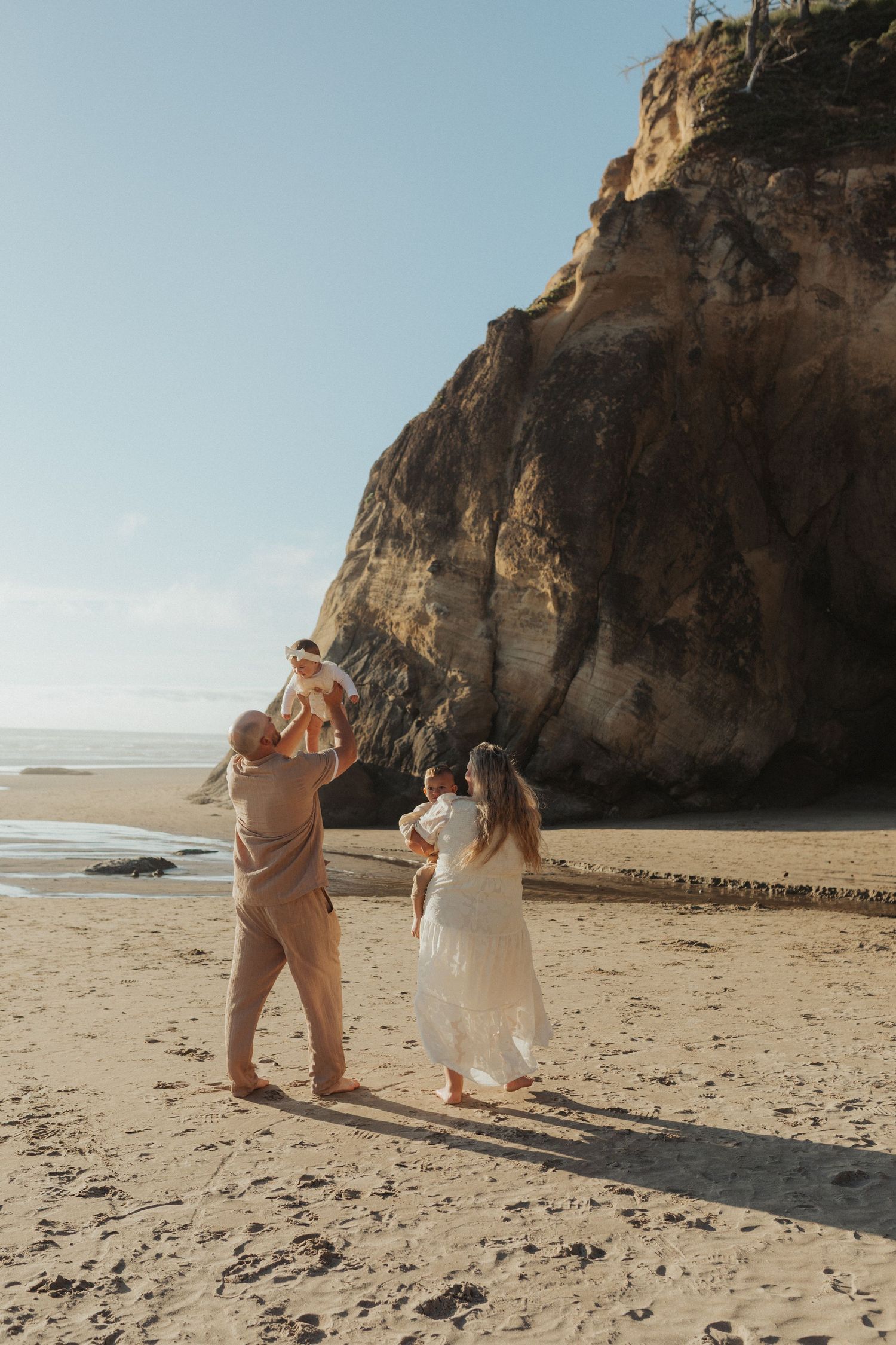 Family of four enjoying a sunny day on the beach near dramatic coastal cliffs in Oregon.