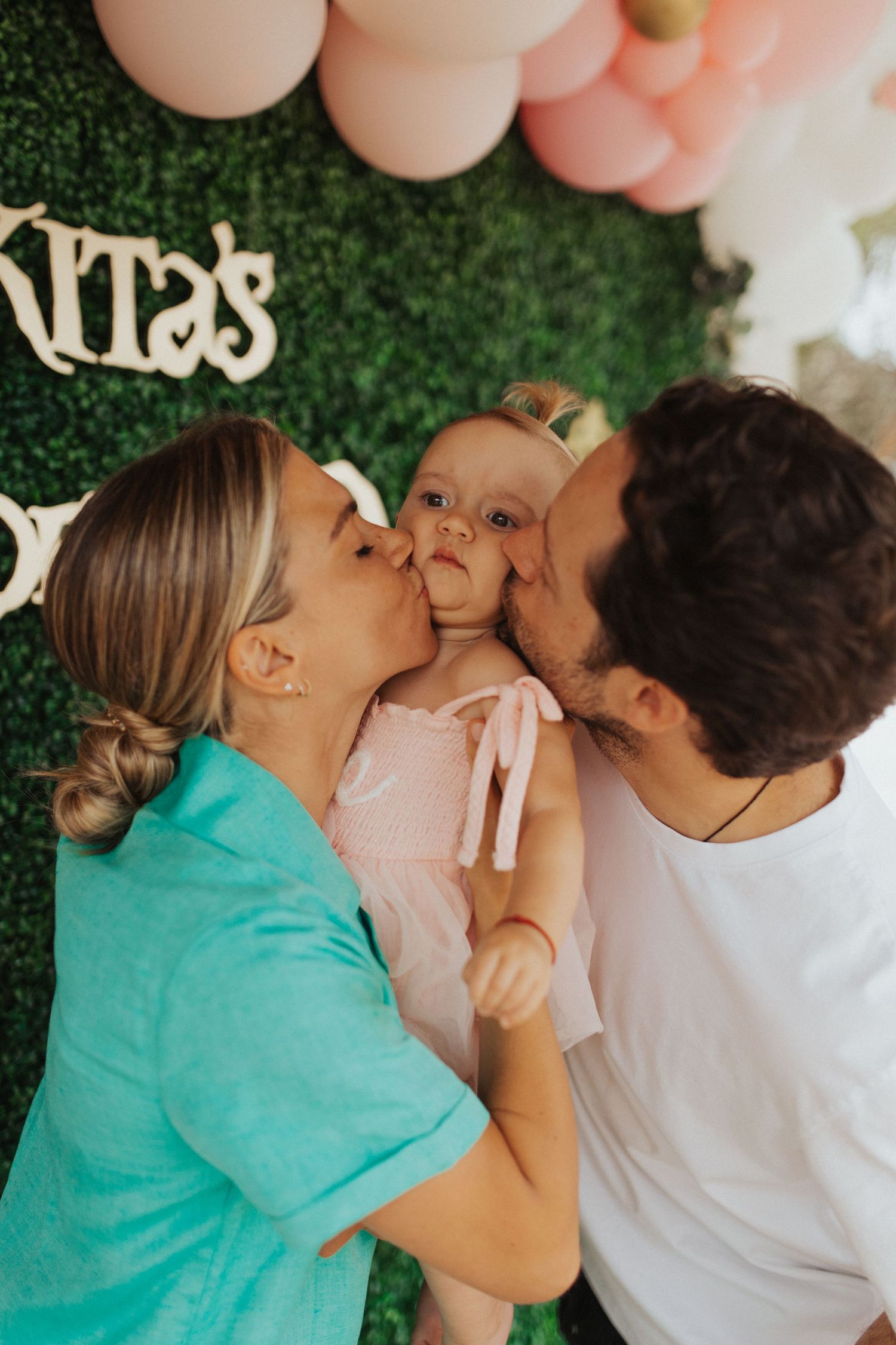Parents kiss baby girl on cheeks at first birthday party.