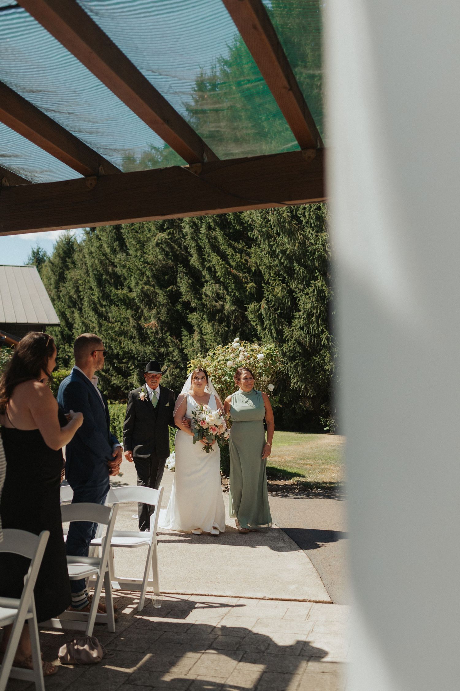 Bride walking down the outdoor aisle in a white gown with a bridesmaid in sage green at a garden wedding.