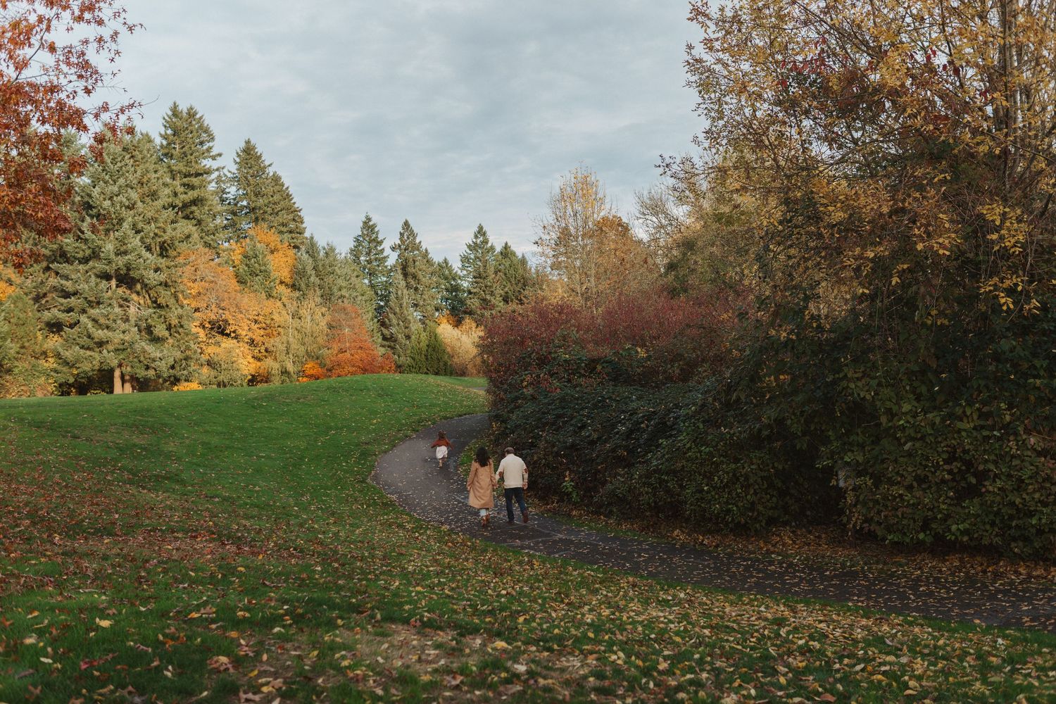 Family walking along a winding park path surrounded by vibrant autumn foliage in fall colors.