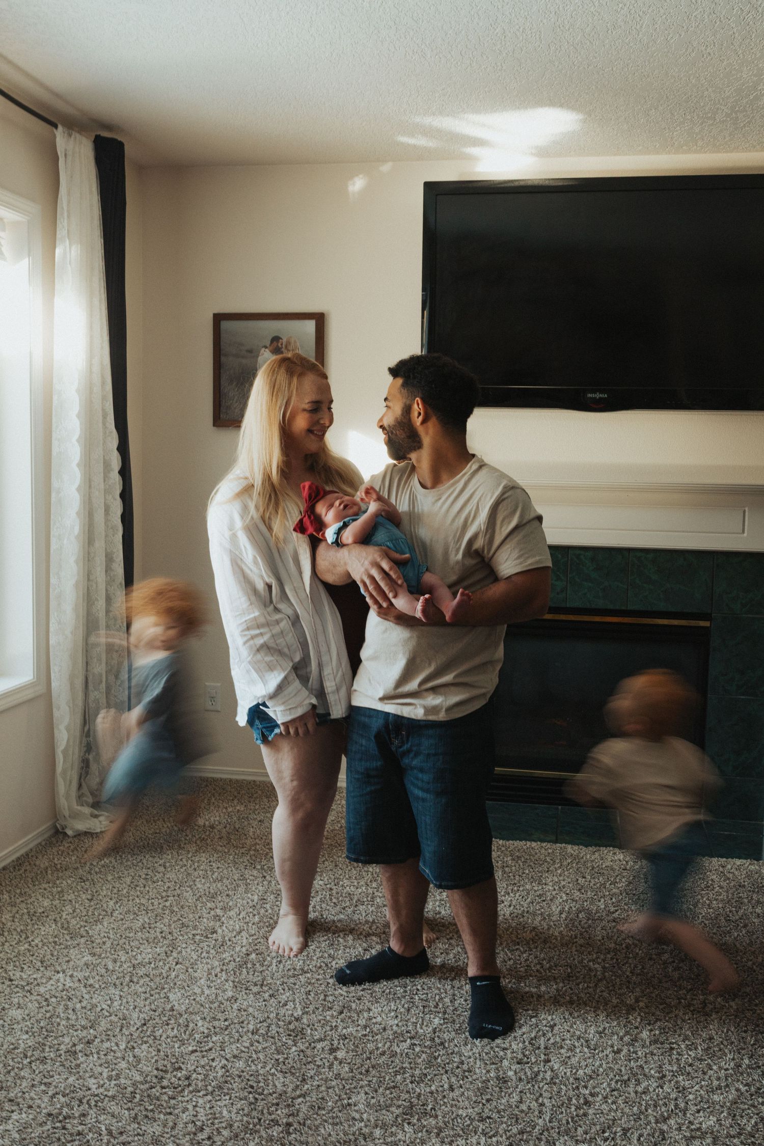 Young family with newborn baby and two blurred children running around their living room.