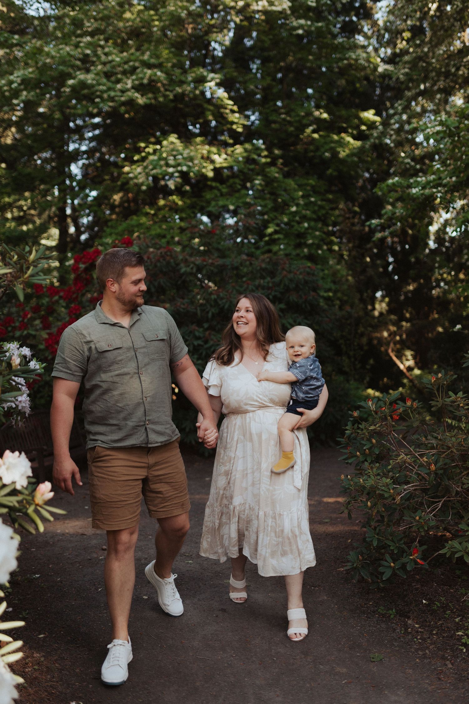 Couple holding hands and walking through garden path while mother carries smiling baby boy.