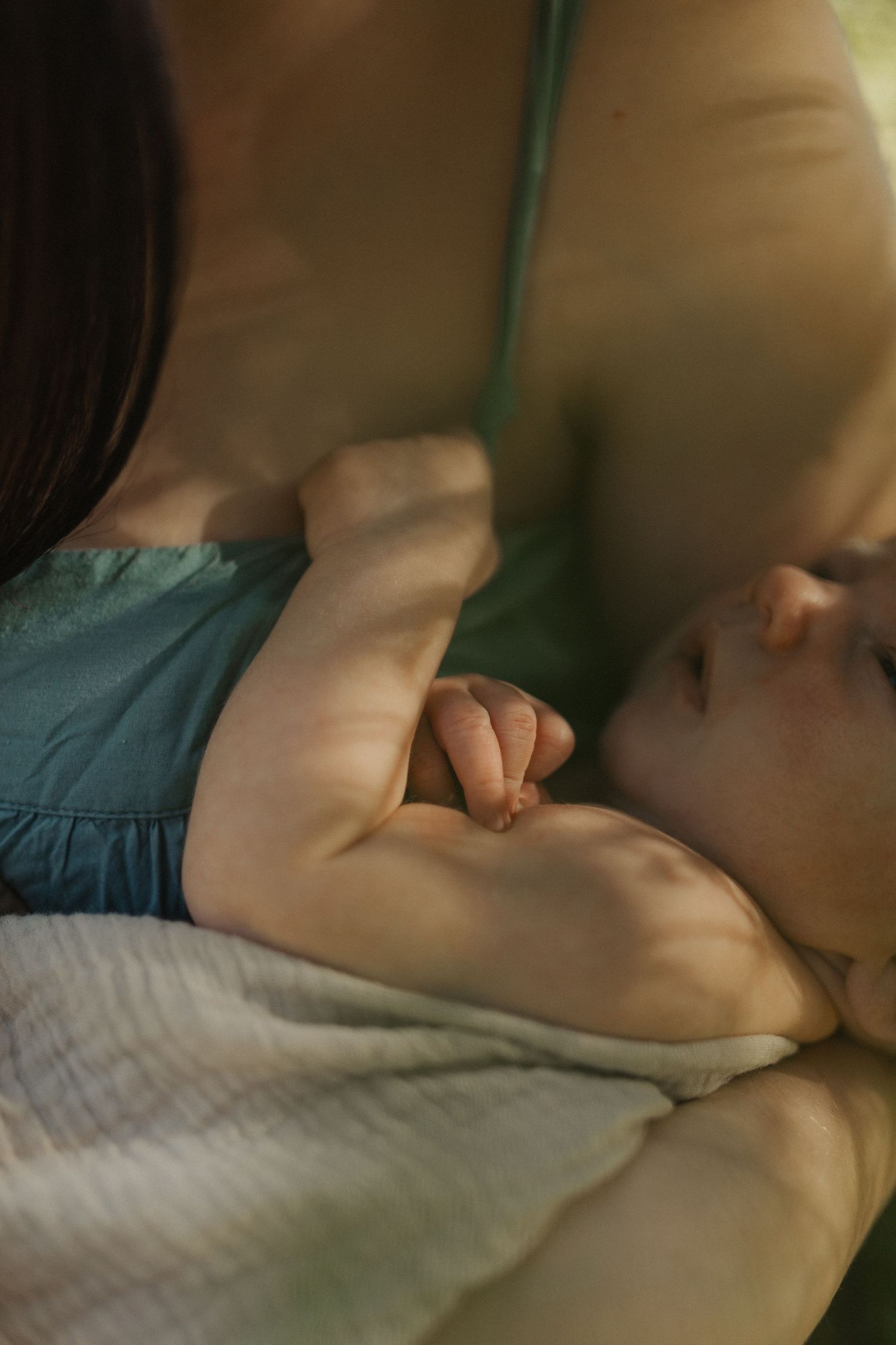 Close-up of sleeping newborn baby breastfeeding while mother in teal dress holds baby gently.