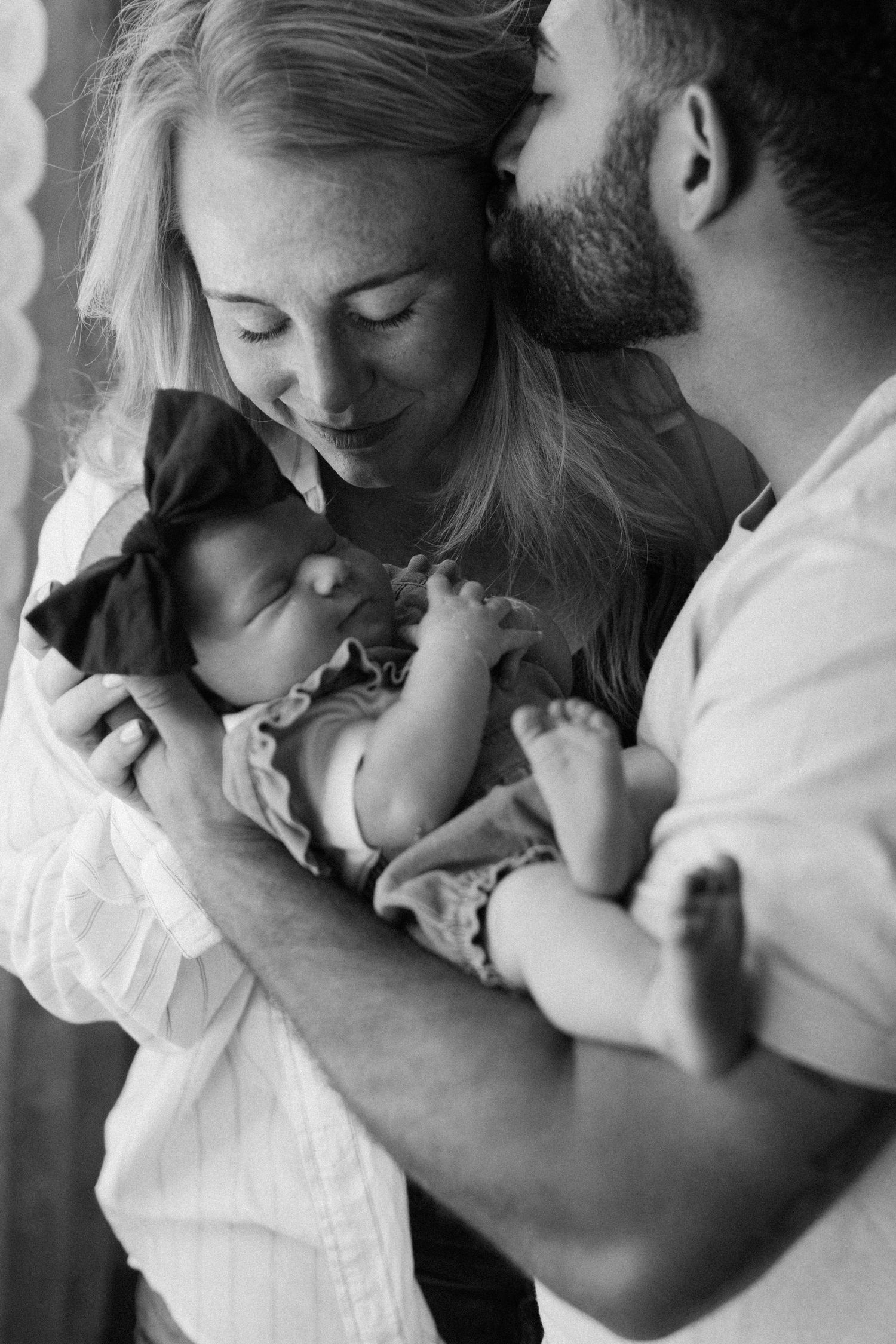 Black and white photo of new parents tenderly holding their sleeping newborn baby close together.