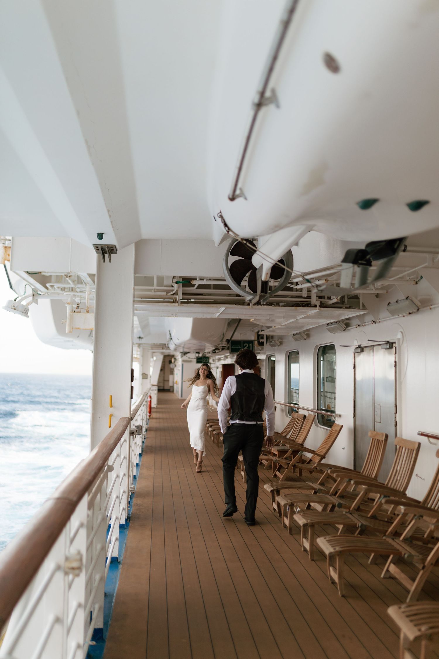 Bride and groom walking hand in hand along the deck of a cruise ship with ocean views.