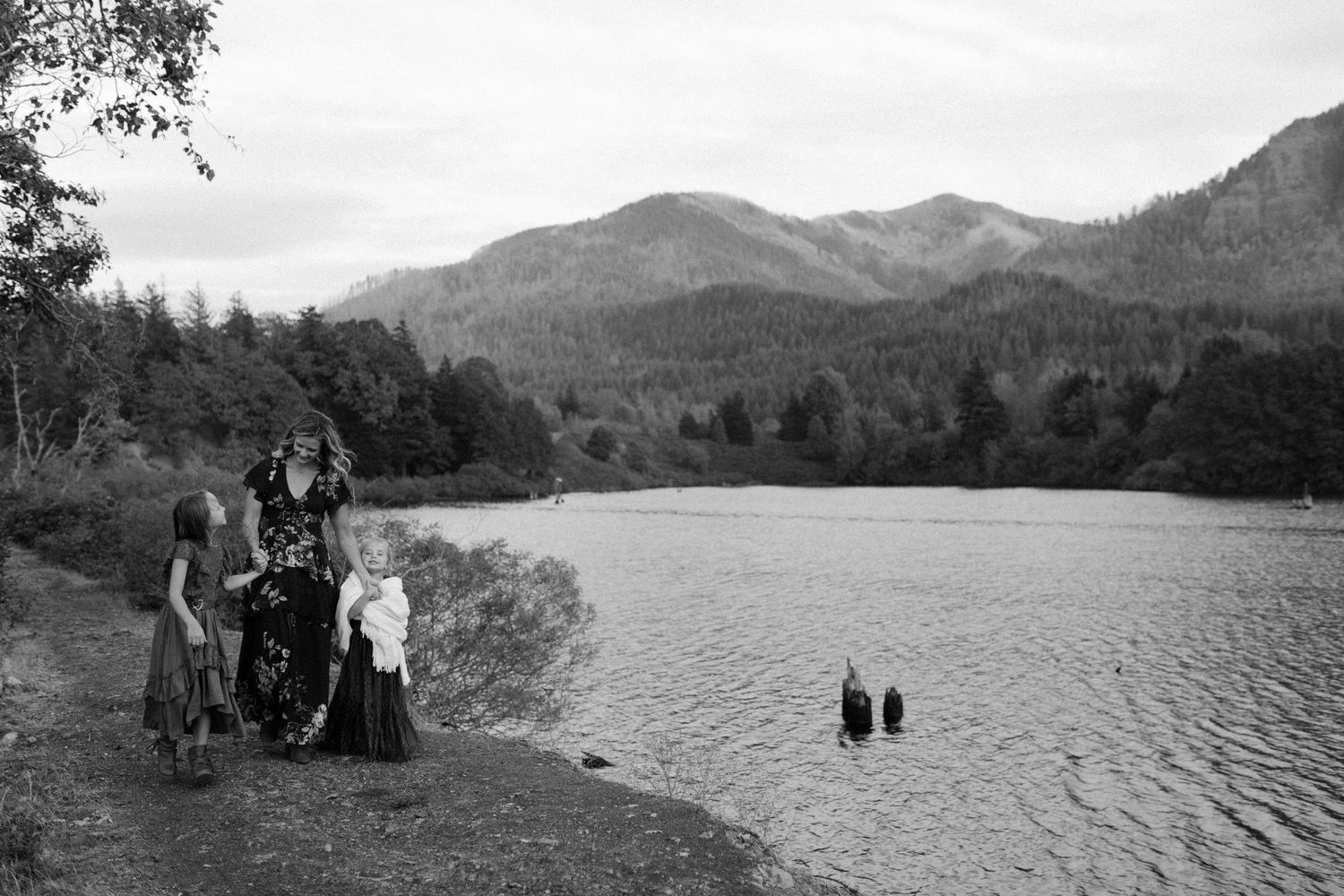 Black and white photo of a mother and two children walking along a scenic mountain lakeside path.
