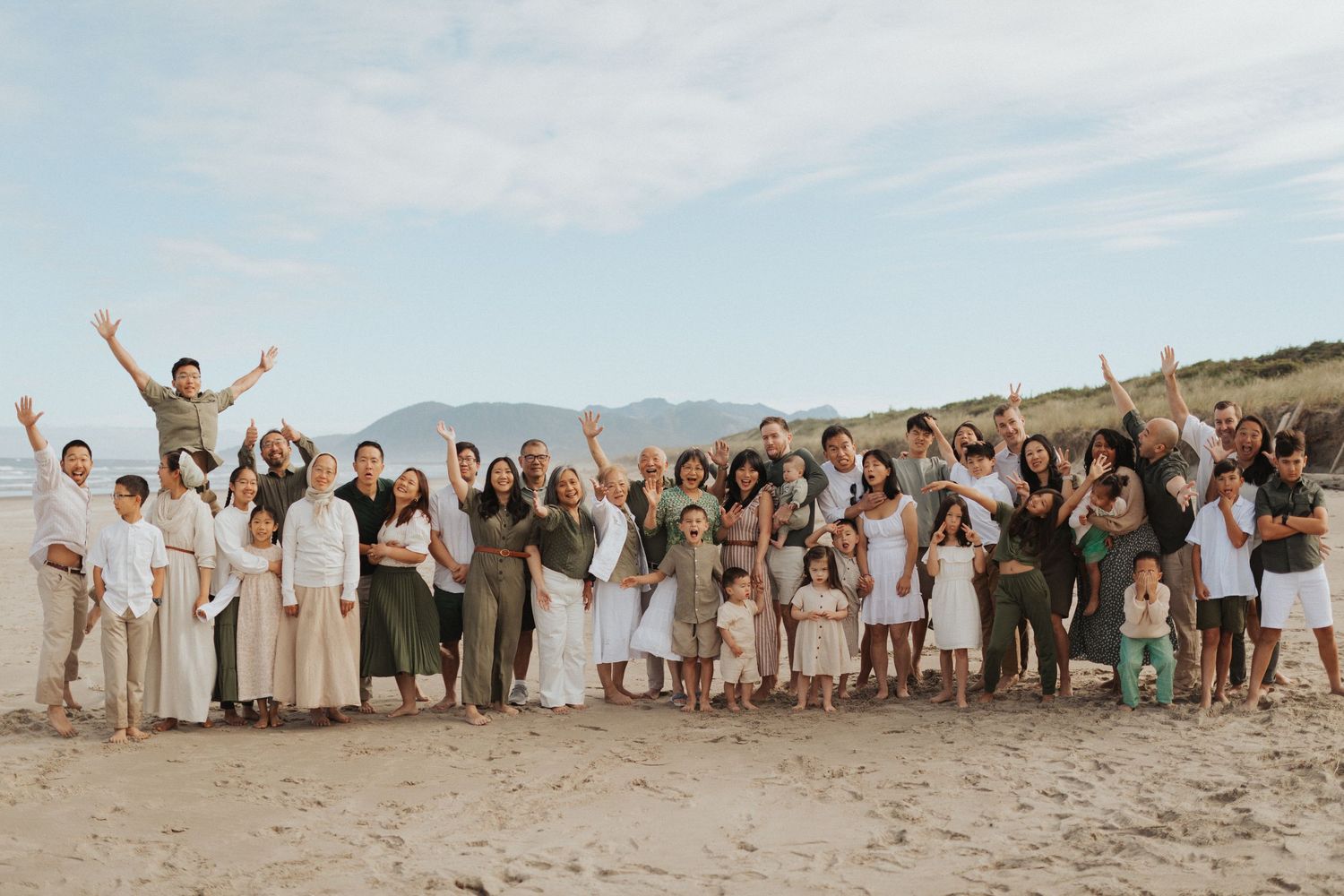 Large extended family group celebrating together on a sandy beach with mountains in the background.