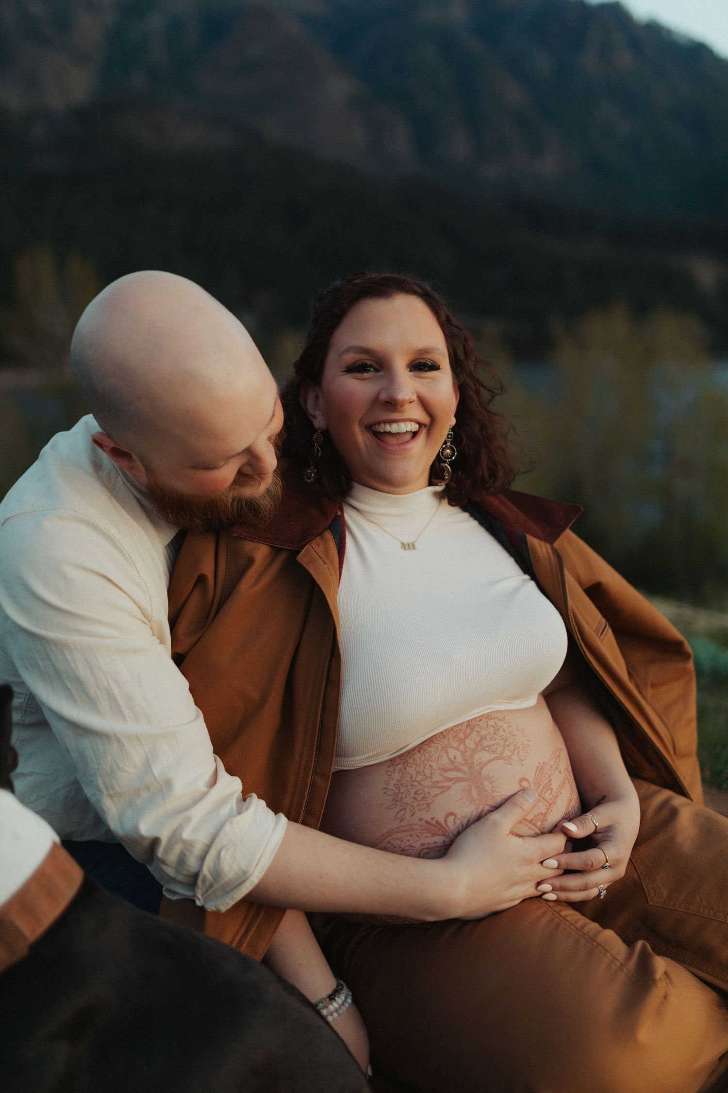 Smiling pregnant woman with belly art embraced by her partner during a golden hour maternity session.