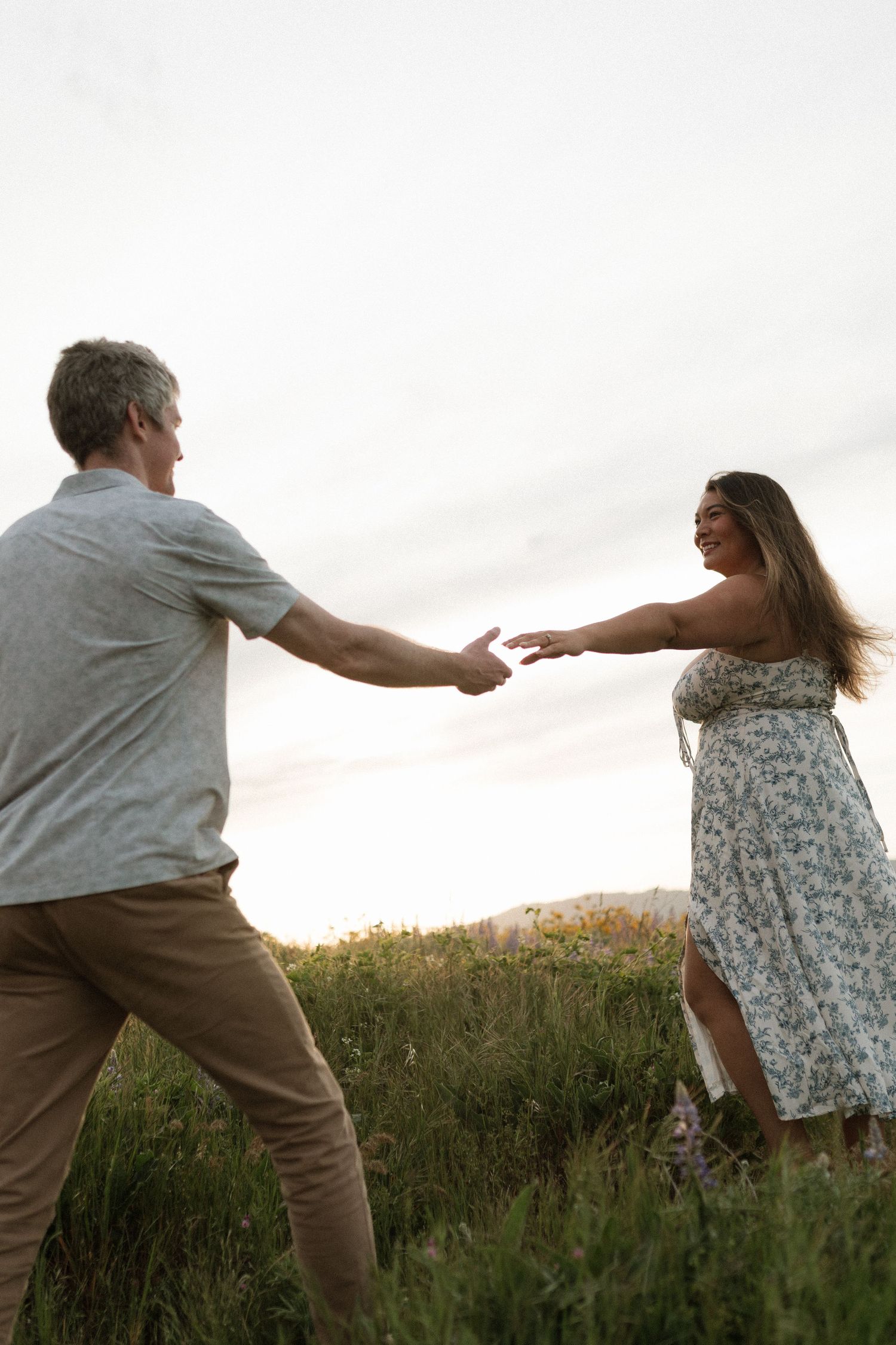 Couple playfully reaching for each other's hands in a wildflower field at sunset.