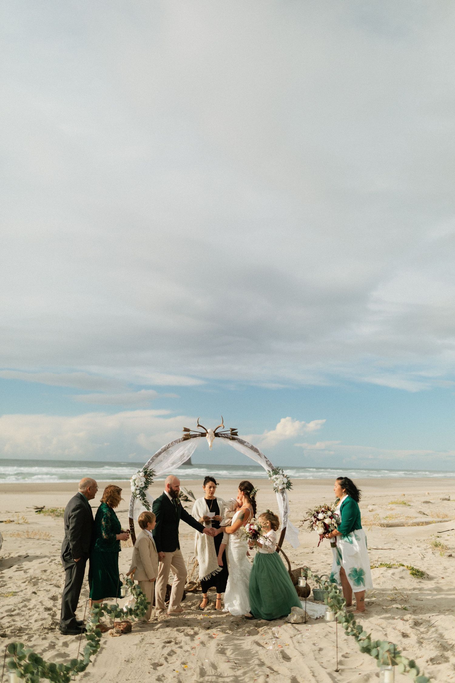 Beach wedding ceremony with couple exchanging vows under a floral arch by the ocean.