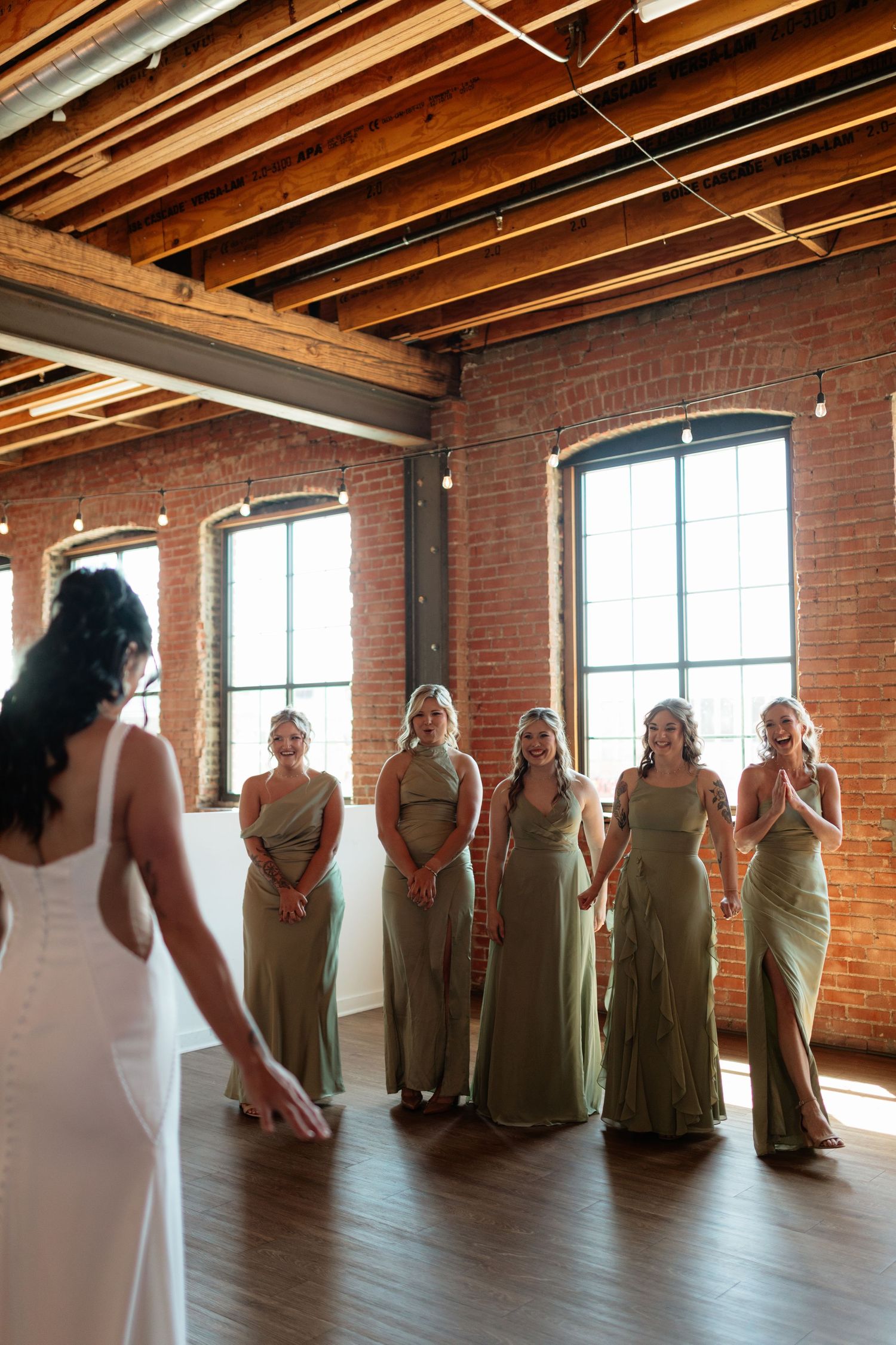 Bridesmaids in sage green gowns react with joy during first look reveal with bride in white dress.