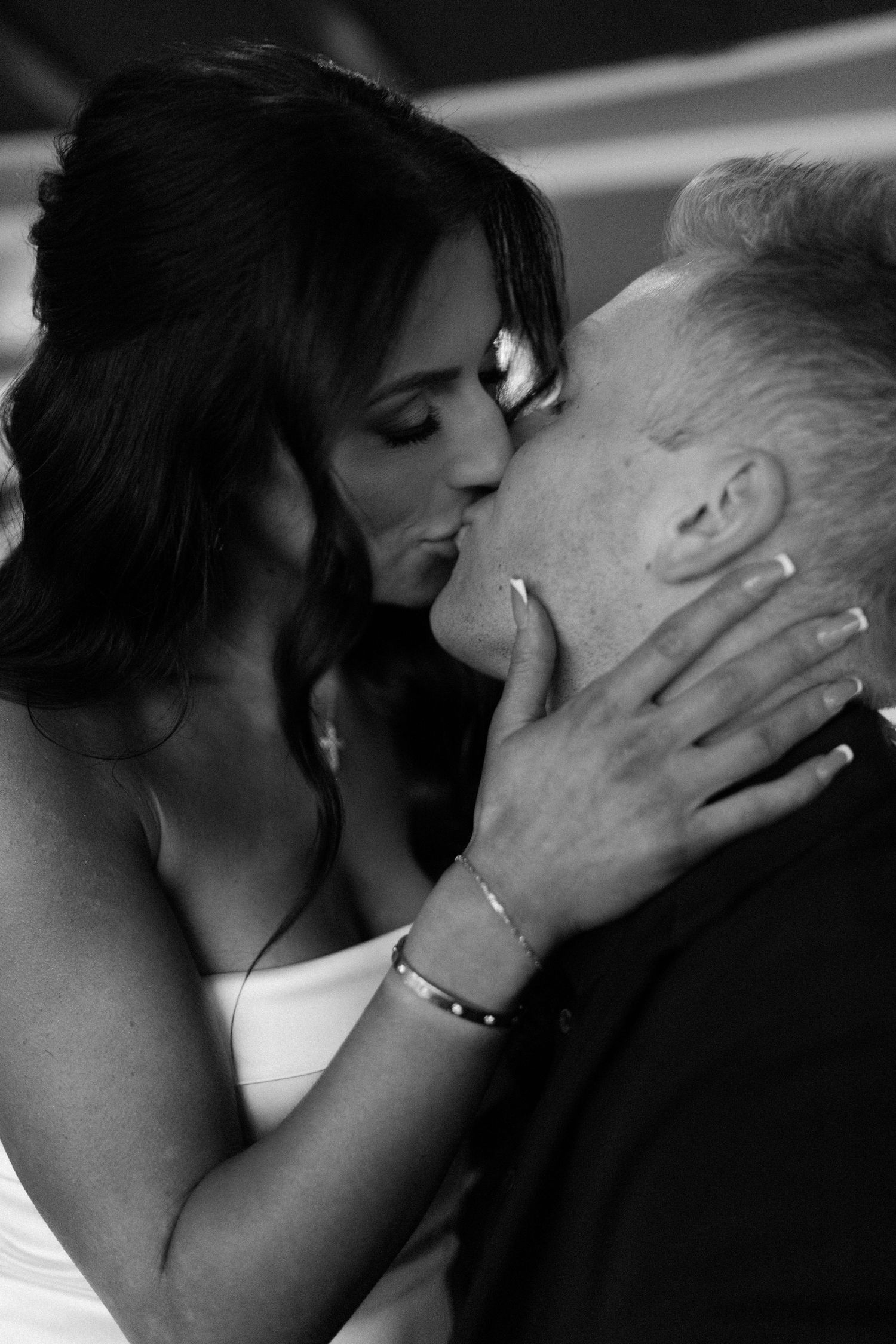 Black and white romantic photo of couple sharing a passionate kiss, woman holding mans face tenderly.