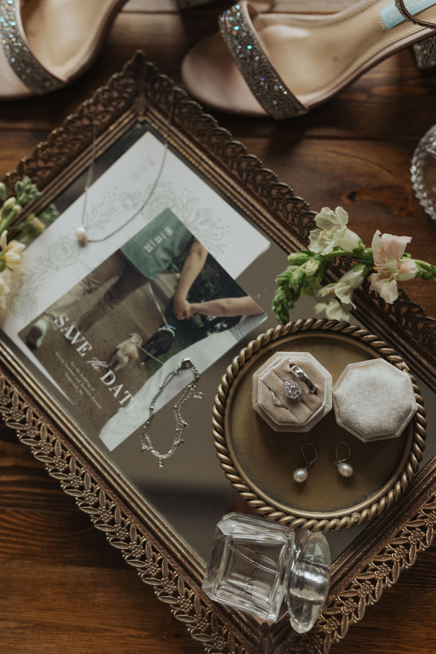 Elegant wedding flat lay featuring save the date card, ring box, jewelry, and heels on a mirrored tray.