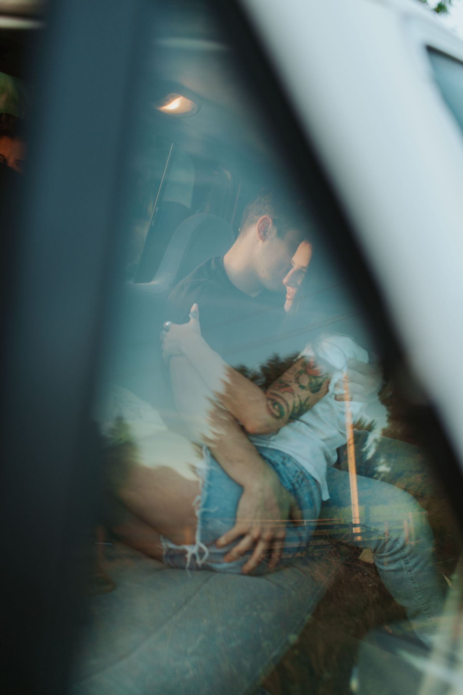 A couple embraces intimately inside a vehicle, viewed through a car window.