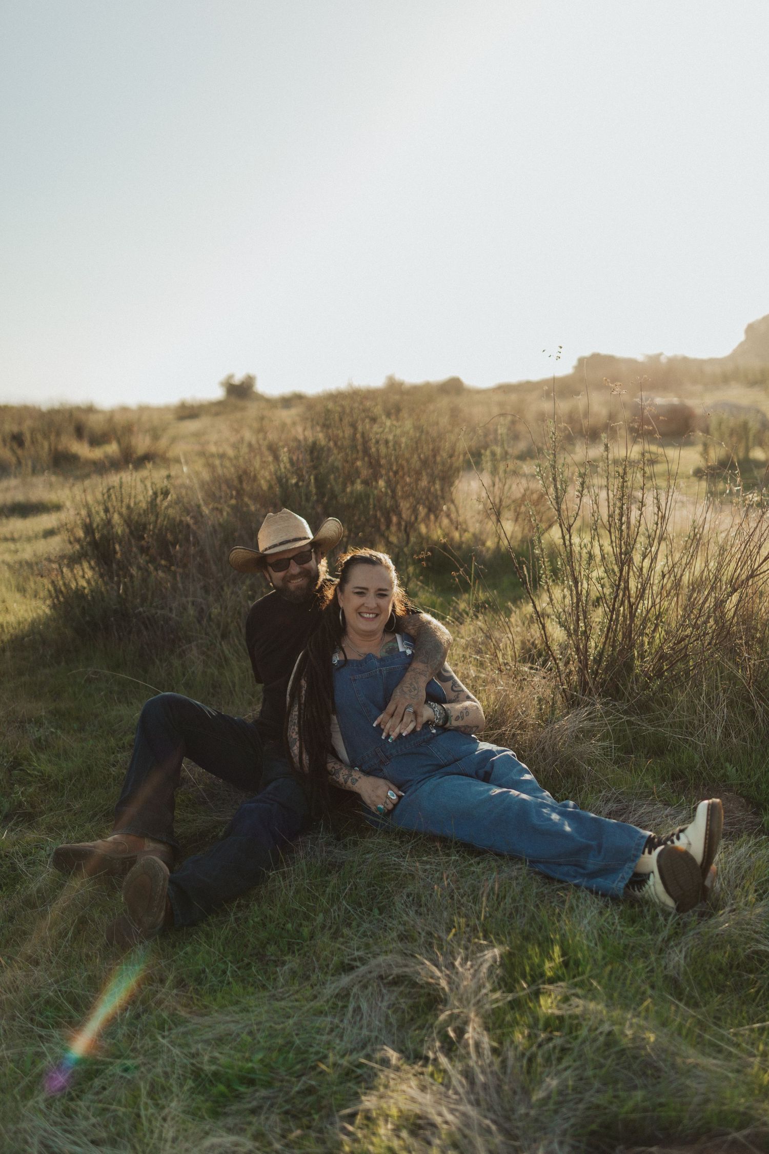 Couple relaxing together in a golden grassy field at sunset with warm lens flare.
