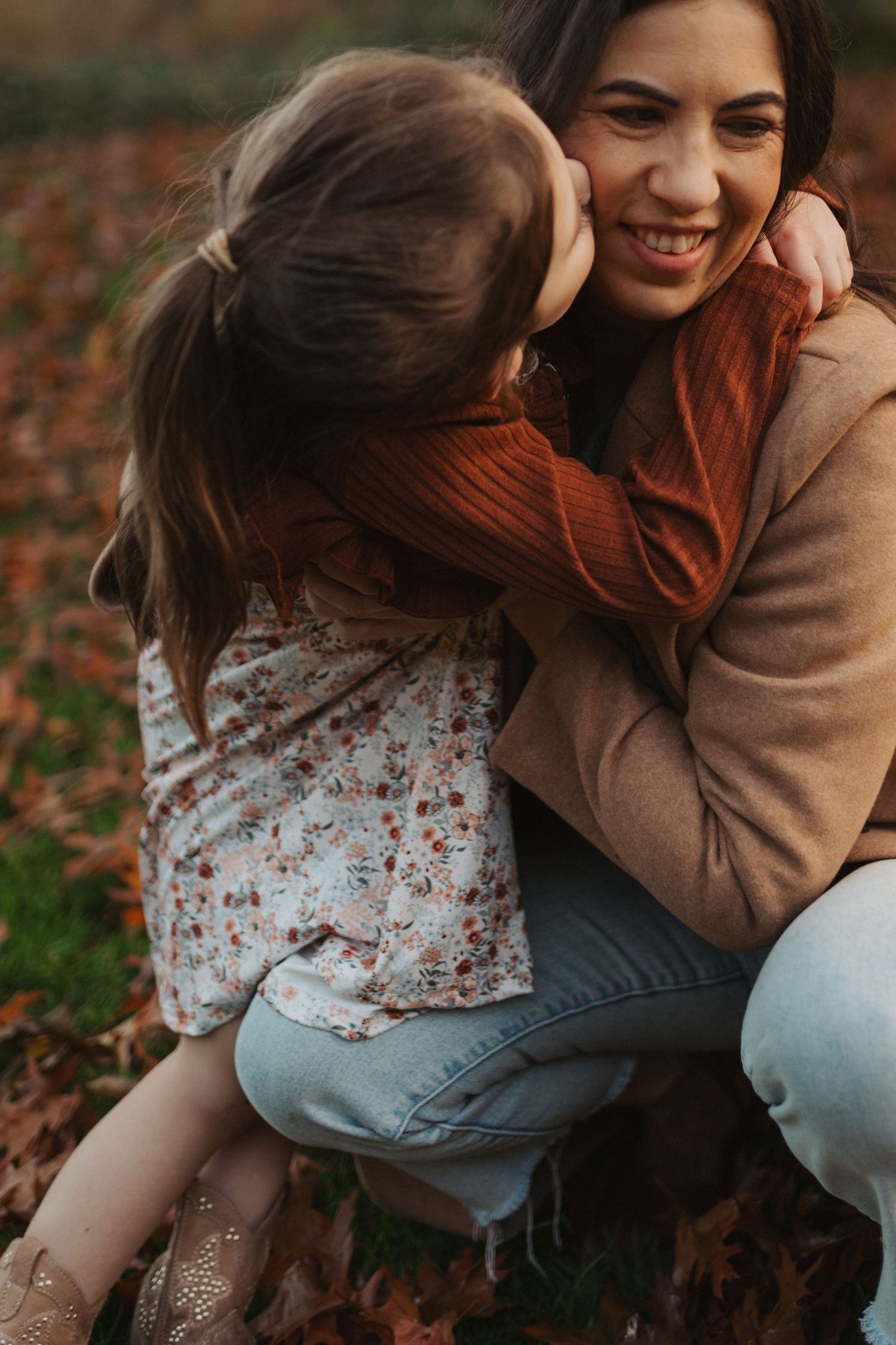 A mother smiles warmly while her young daughter wraps her arms around her neck in a loving embrace.