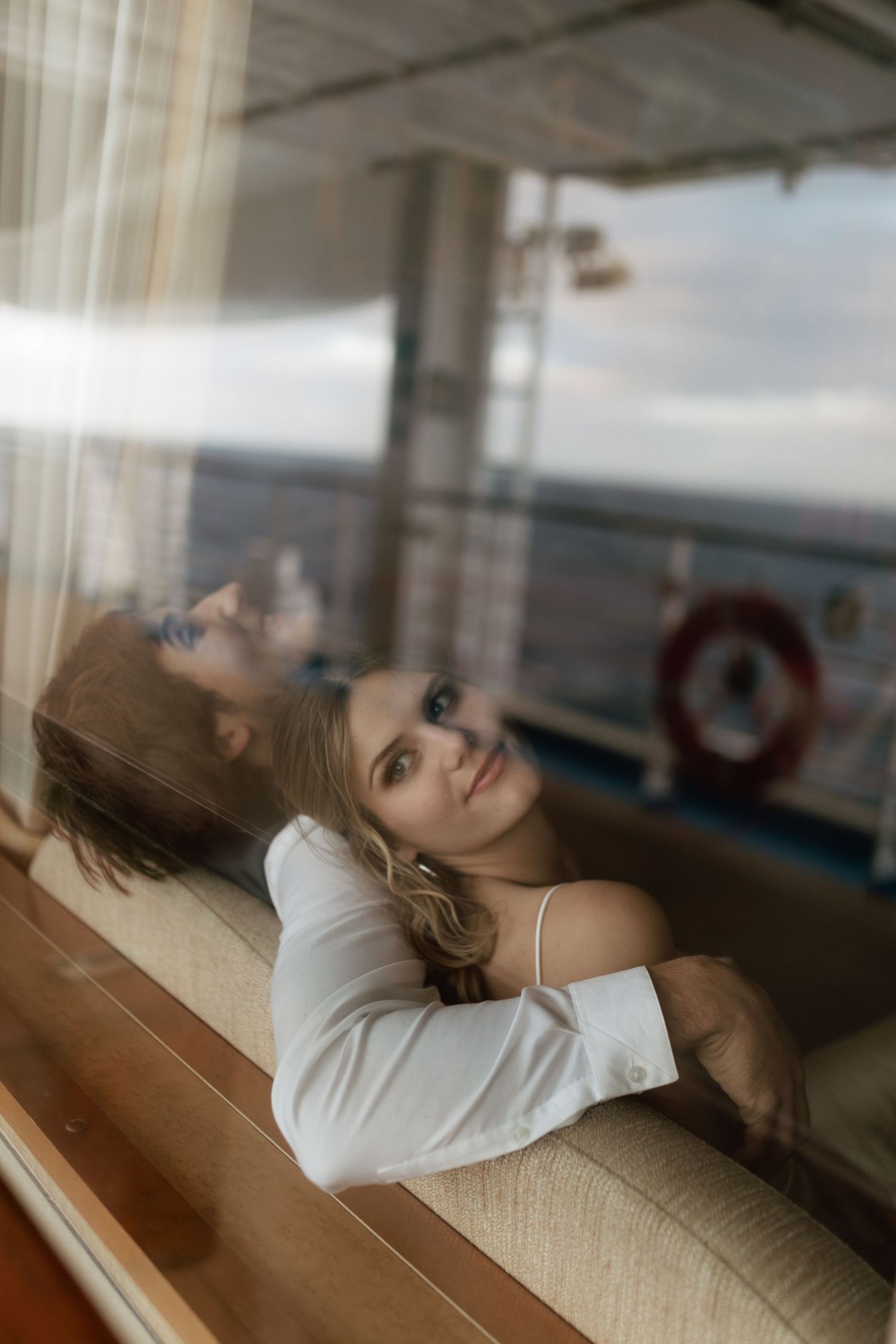 Bride gazing upward while relaxing on a couch beside a cruise ship cabin window.