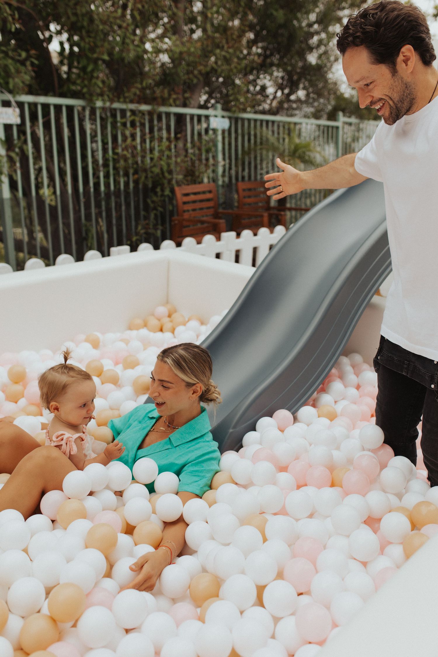 Family plays in white ball pit with gray slide outdoors.