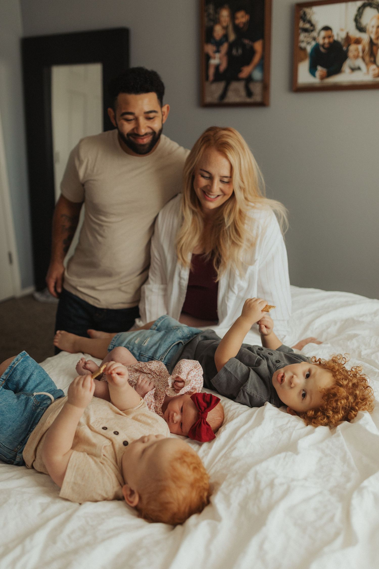 A smiling family with three young children relaxes together on a white bed in a decorated bedroom.