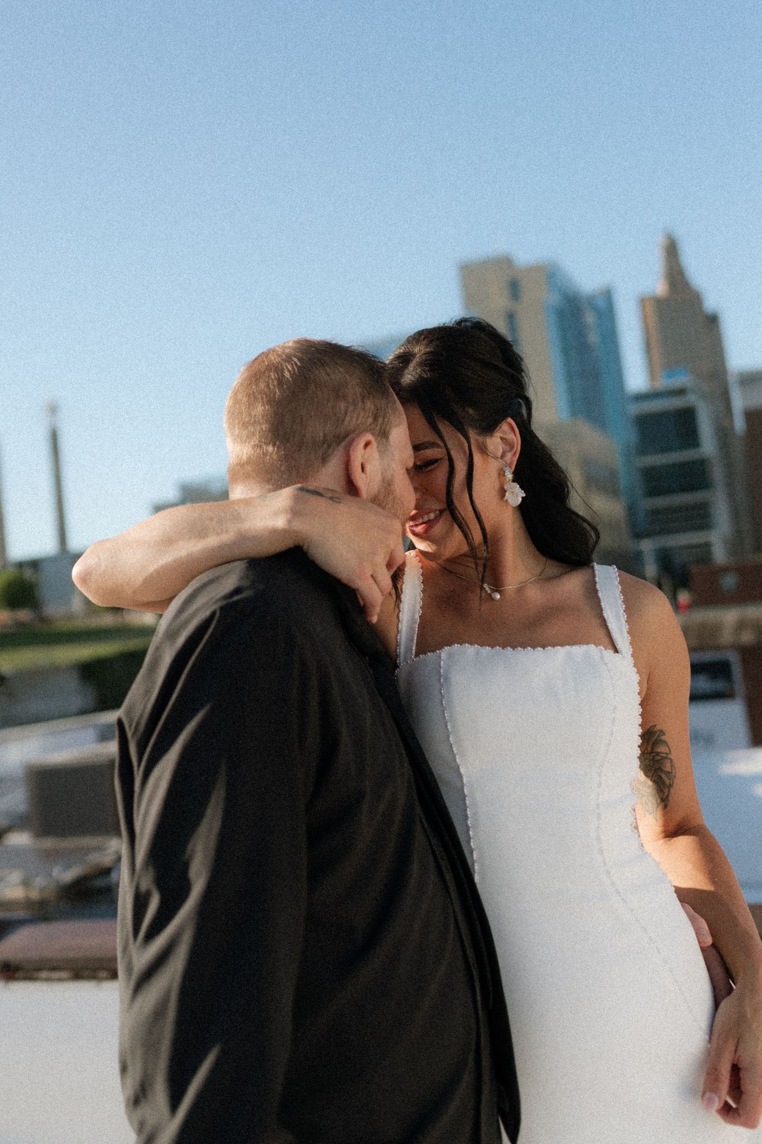 A bride and groom share an intimate moment on a rooftop with a city skyline backdrop on their wedding day.