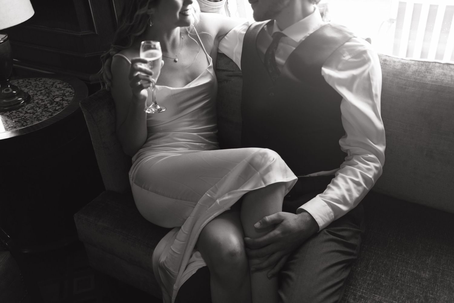 Black and white photo of couple sharing champagne while seated together in an intimate setting.