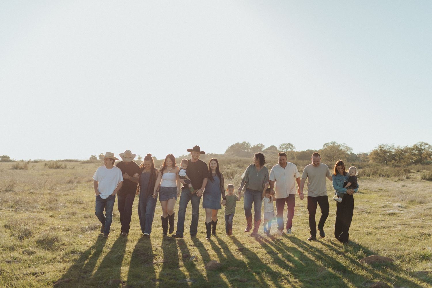 Large extended family of ten walking together across a sunlit open field with clear sky.