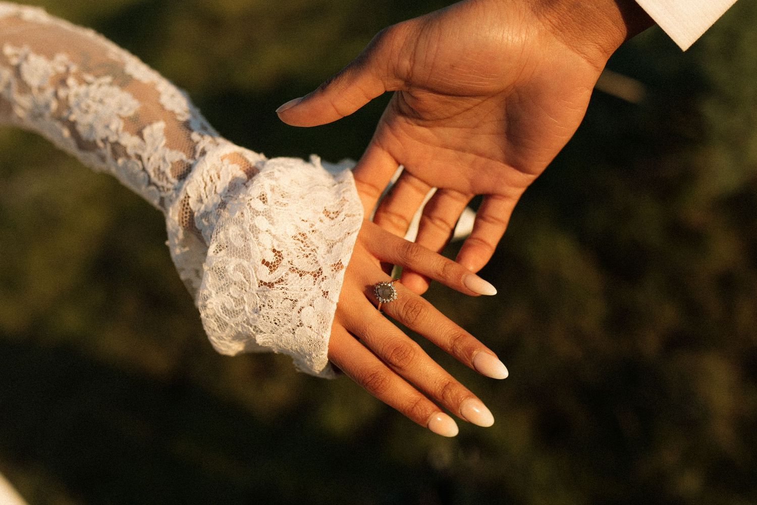 Close-up of bride and groom holding hands showing wedding rings, bride wearing lace sleeve wedding dress.