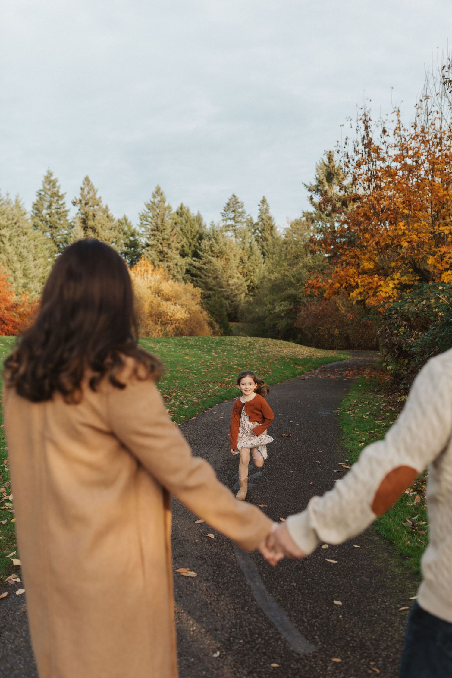 Young girl running toward her parents on a colorful autumn park path during a family photo session.