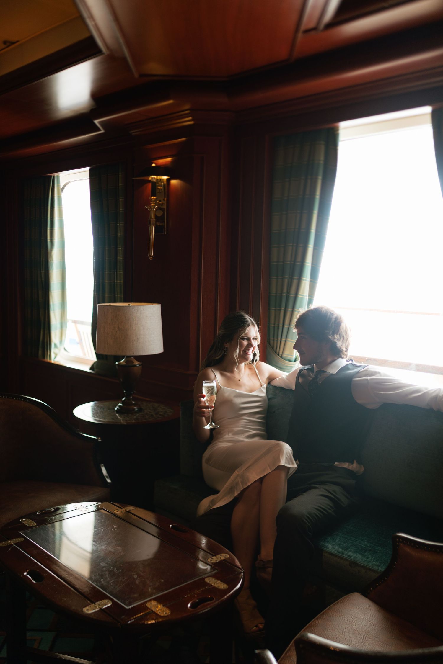 Newlyweds share champagne in a luxurious vintage train car with green curtains and warm lighting.