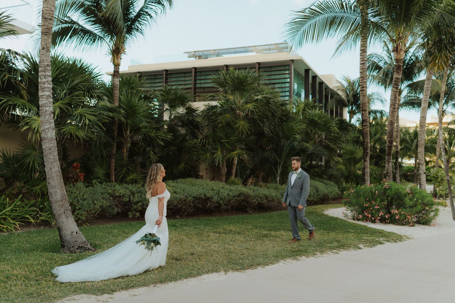 Bride and groom share a romantic first look among tropical palm trees at a luxury beach resort wedding venue.
