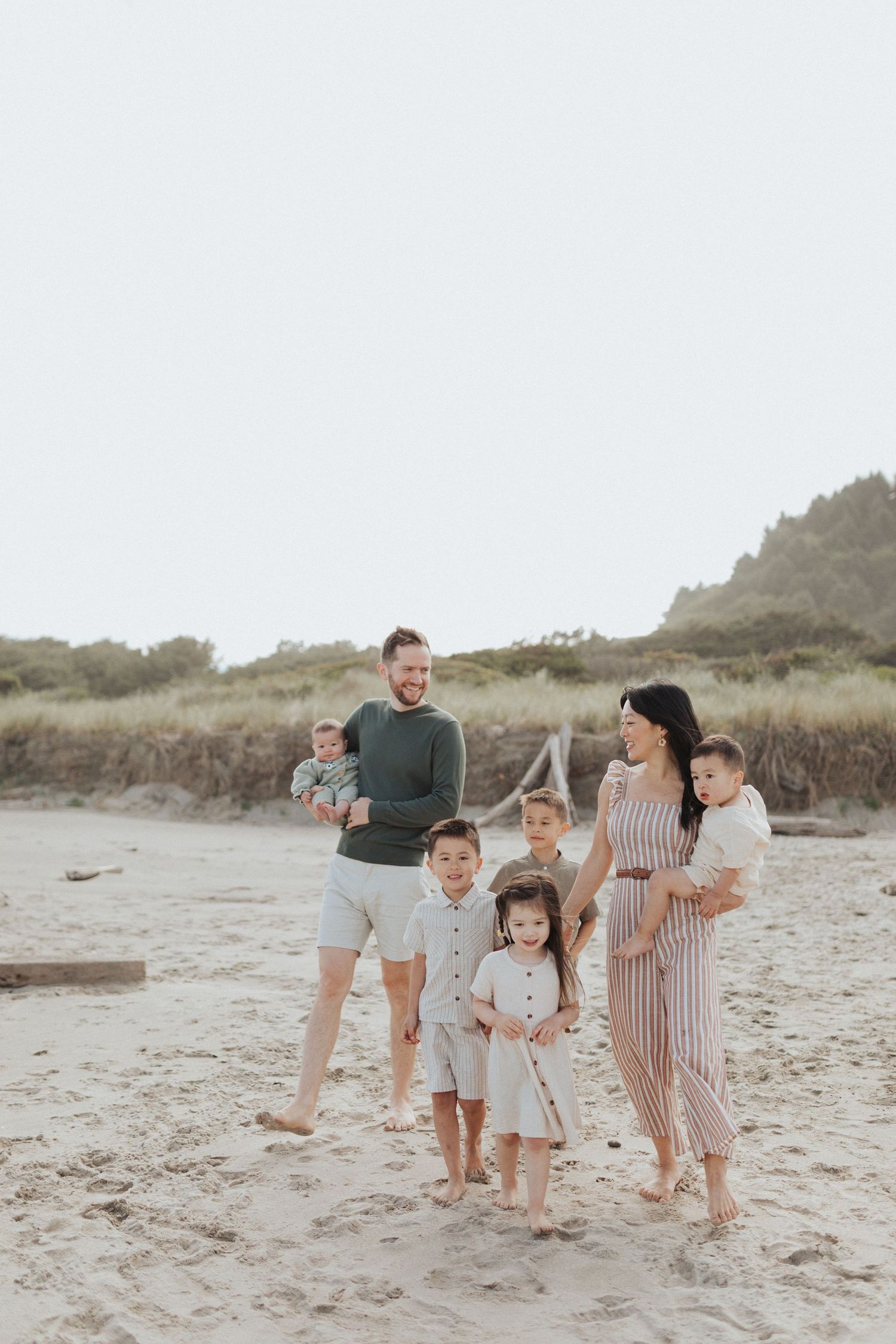 Large family of seven with five young children posing together on a sandy beach at dusk.