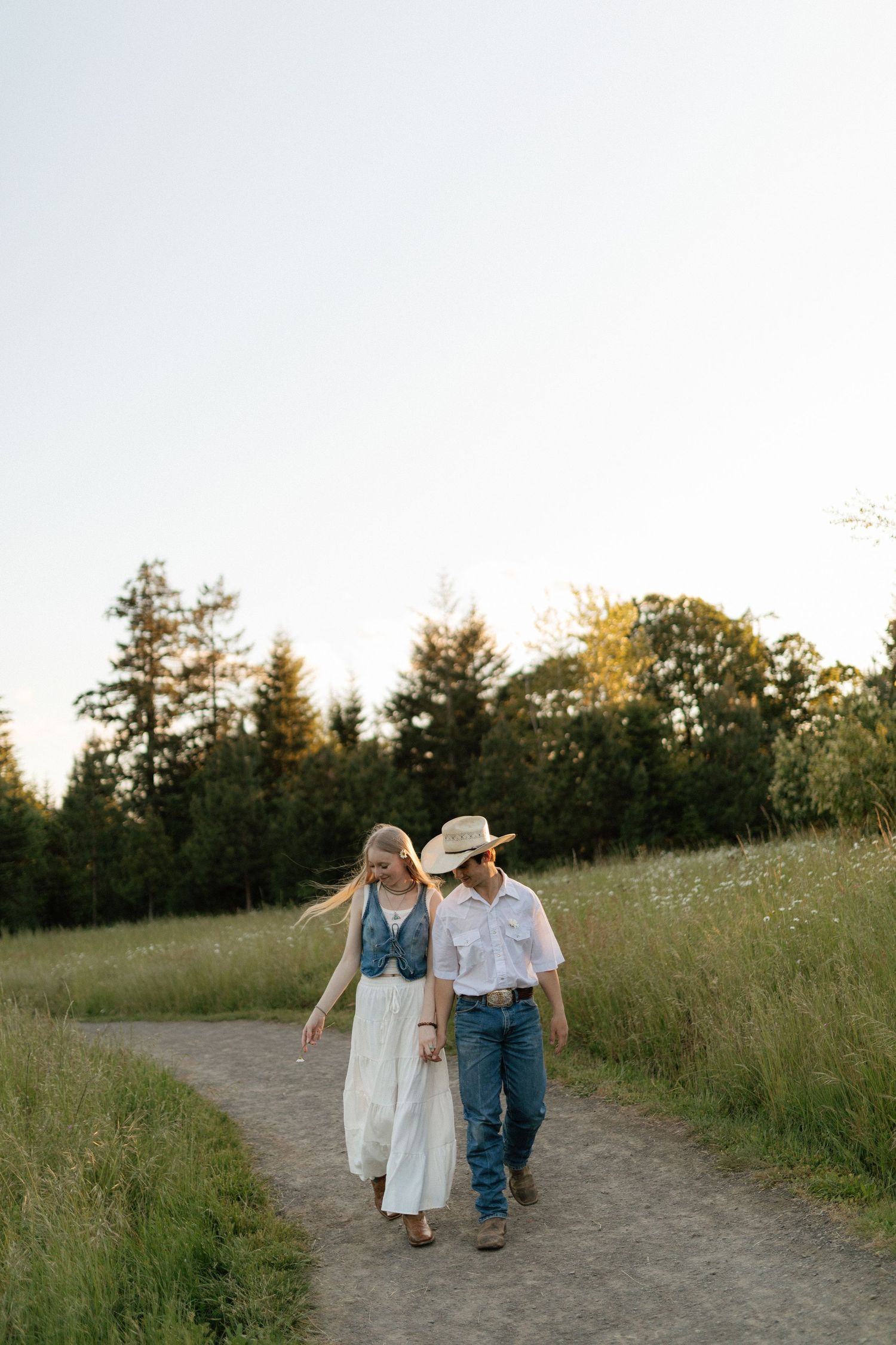 Couple walking together on a winding path through a green meadow at golden hour sunset.