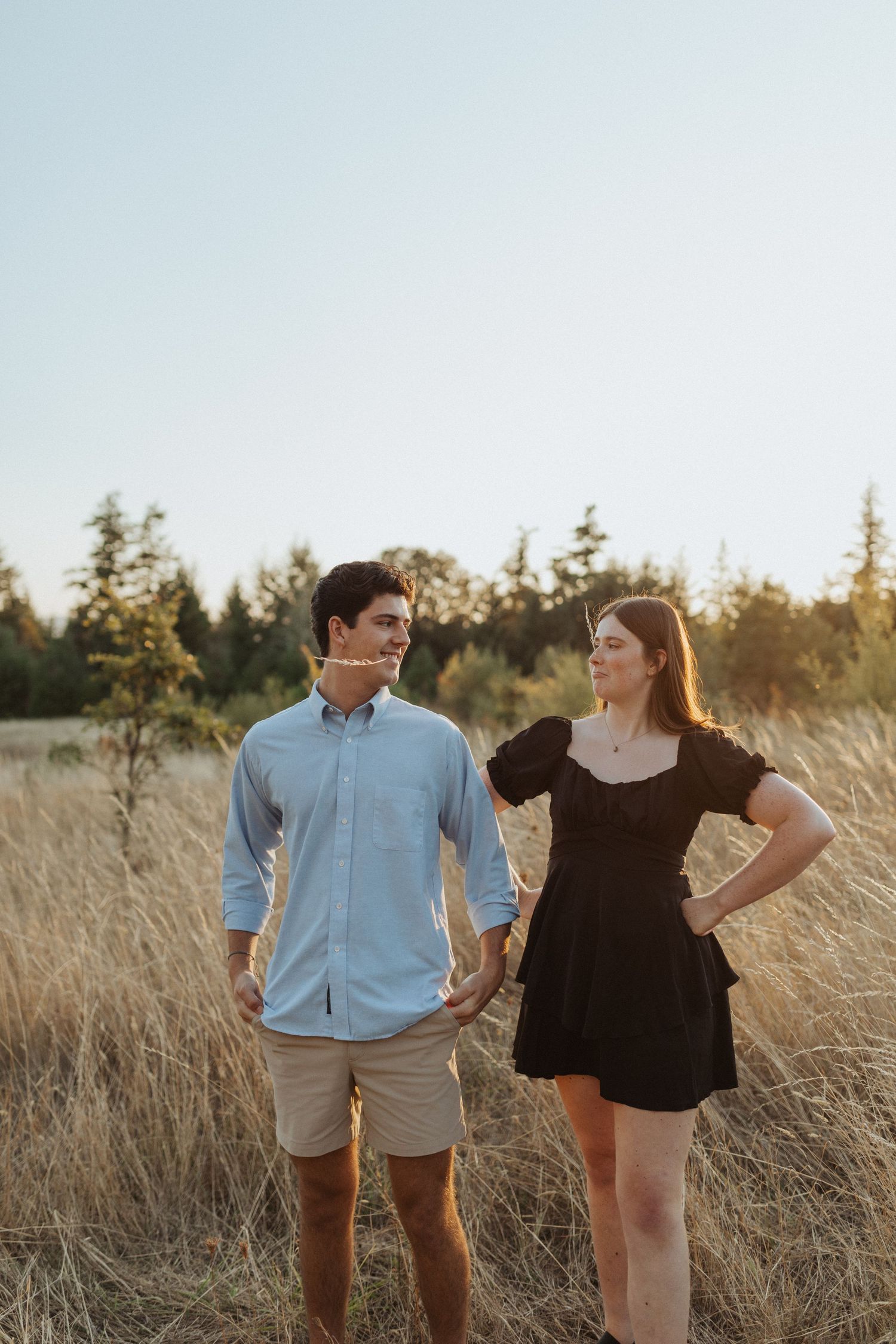 Young man and woman standing together in a golden field at sunset.