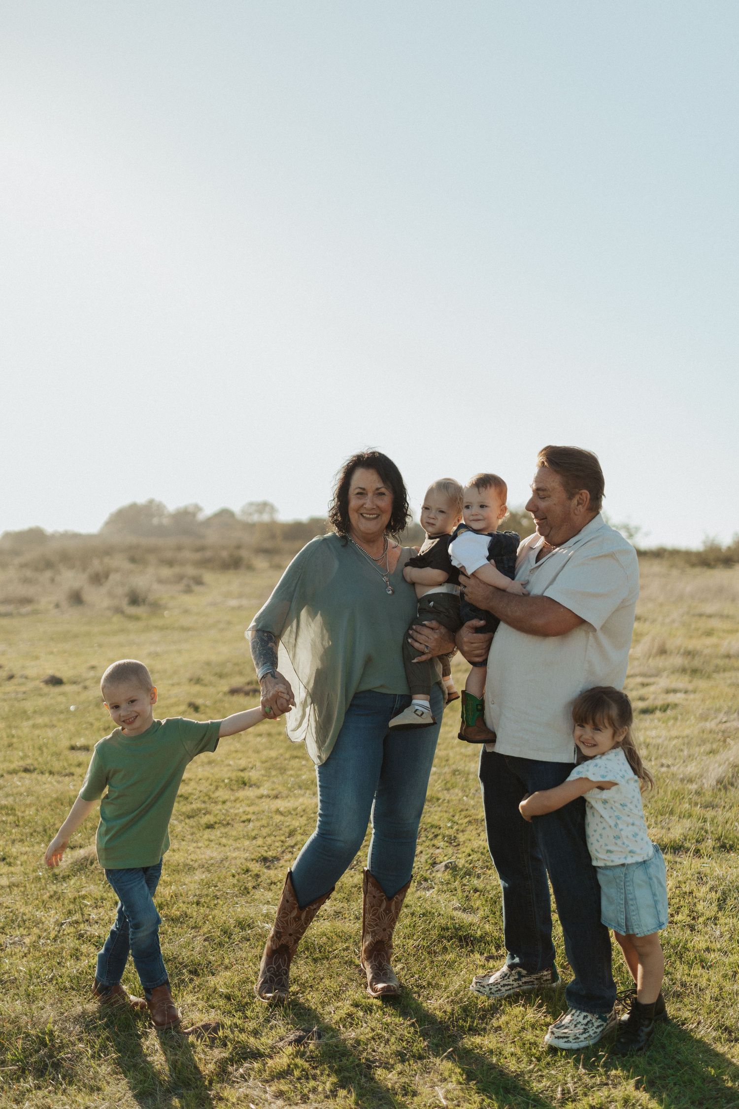 Happy family with grandparents and three young children playing in a sunny green meadow.