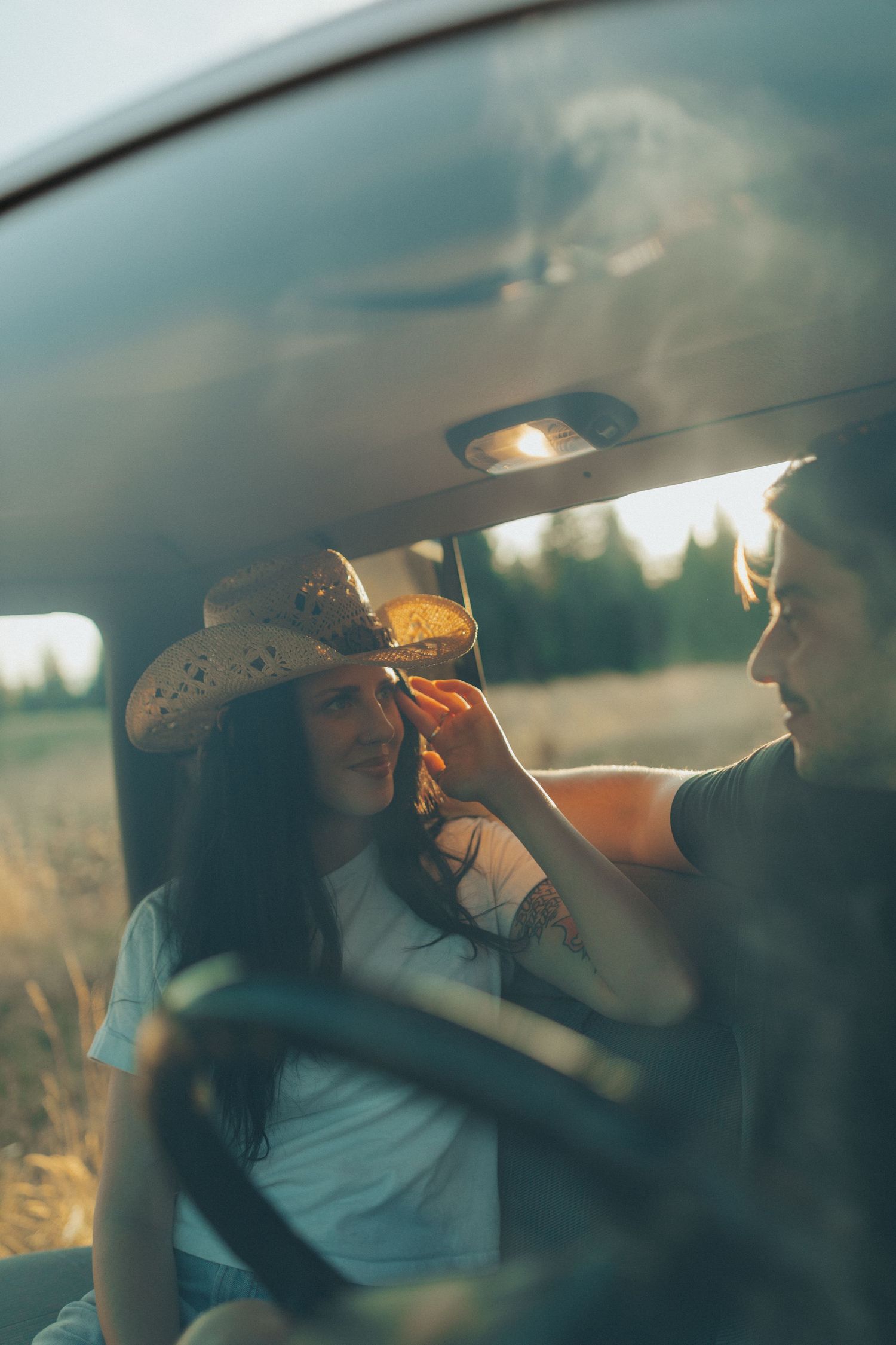 A couple shares an intimate moment inside a vintage truck cab, with the woman in a cowboy hat smiling.