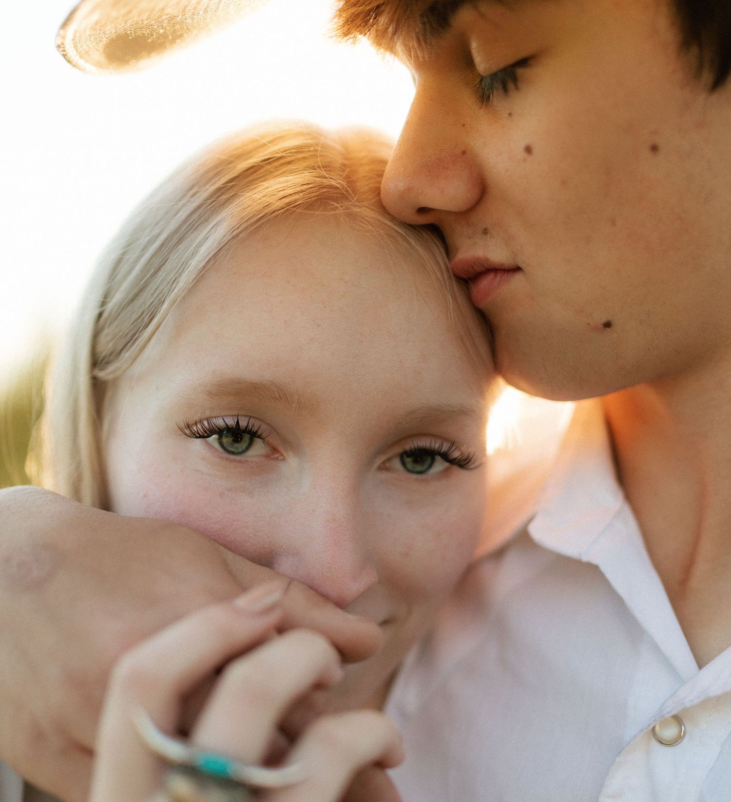 Close-up of young couple sharing tender moment, man kissing woman on head in warm sunset light.