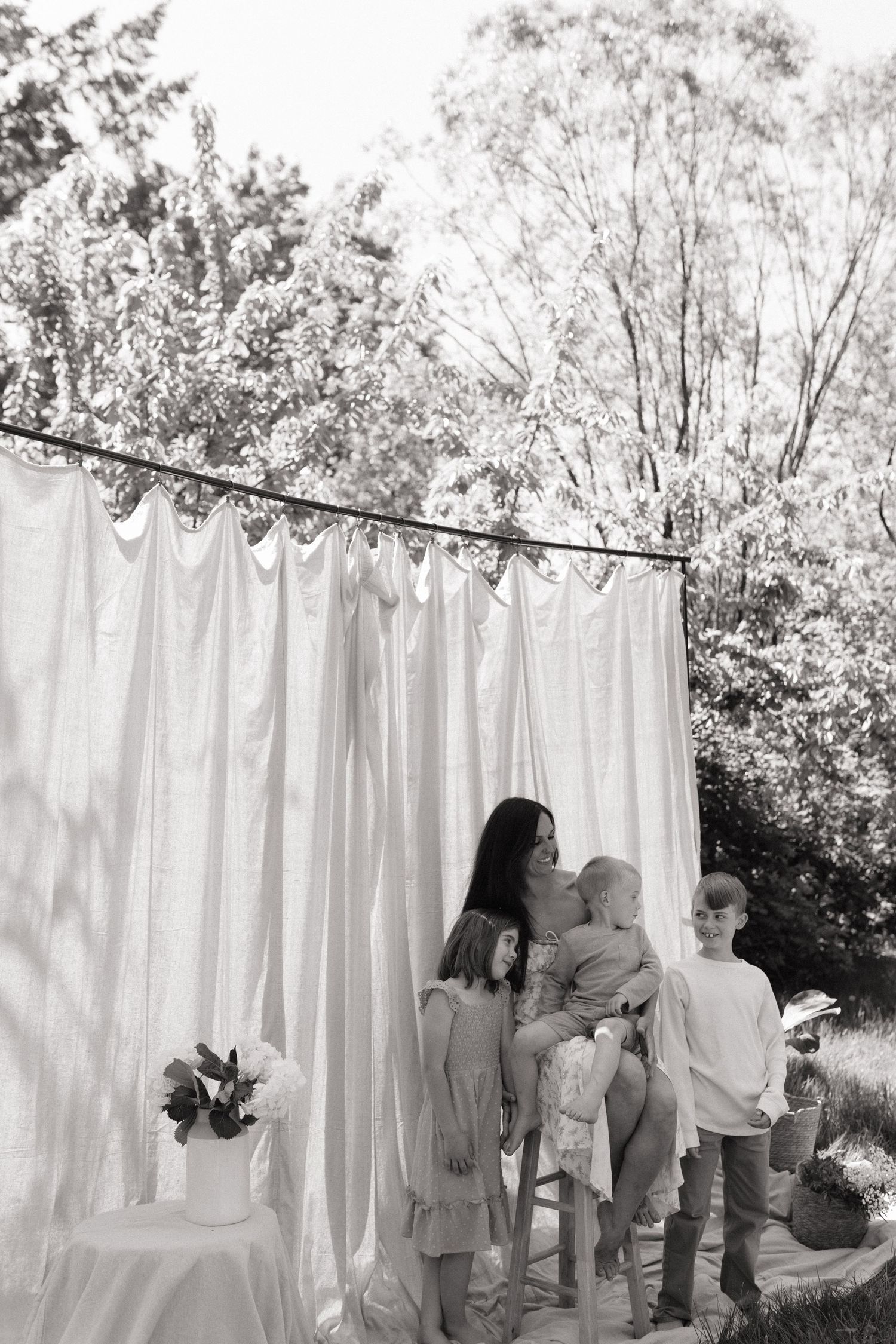 Black and white photo of a mother kissing her toddler while two children stand beside her outdoors.