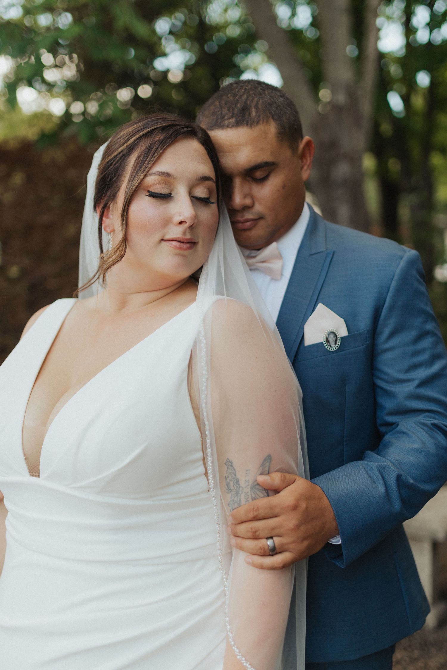 Groom tenderly embraces bride from behind as she closes her eyes in a romantic outdoor wedding portrait.