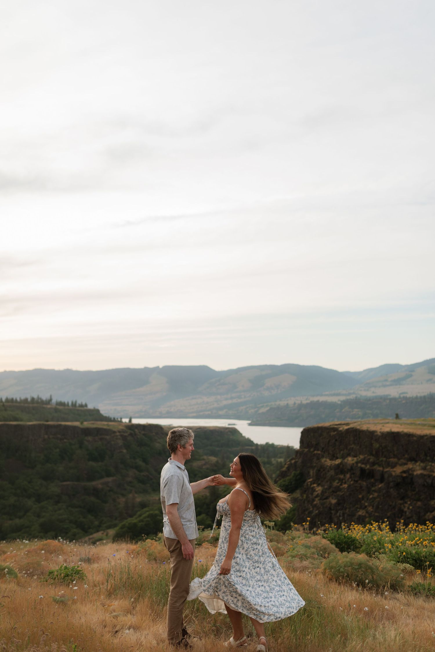 Couple dances playfully in golden field with stunning Columbia River Gorge landscape behind them.