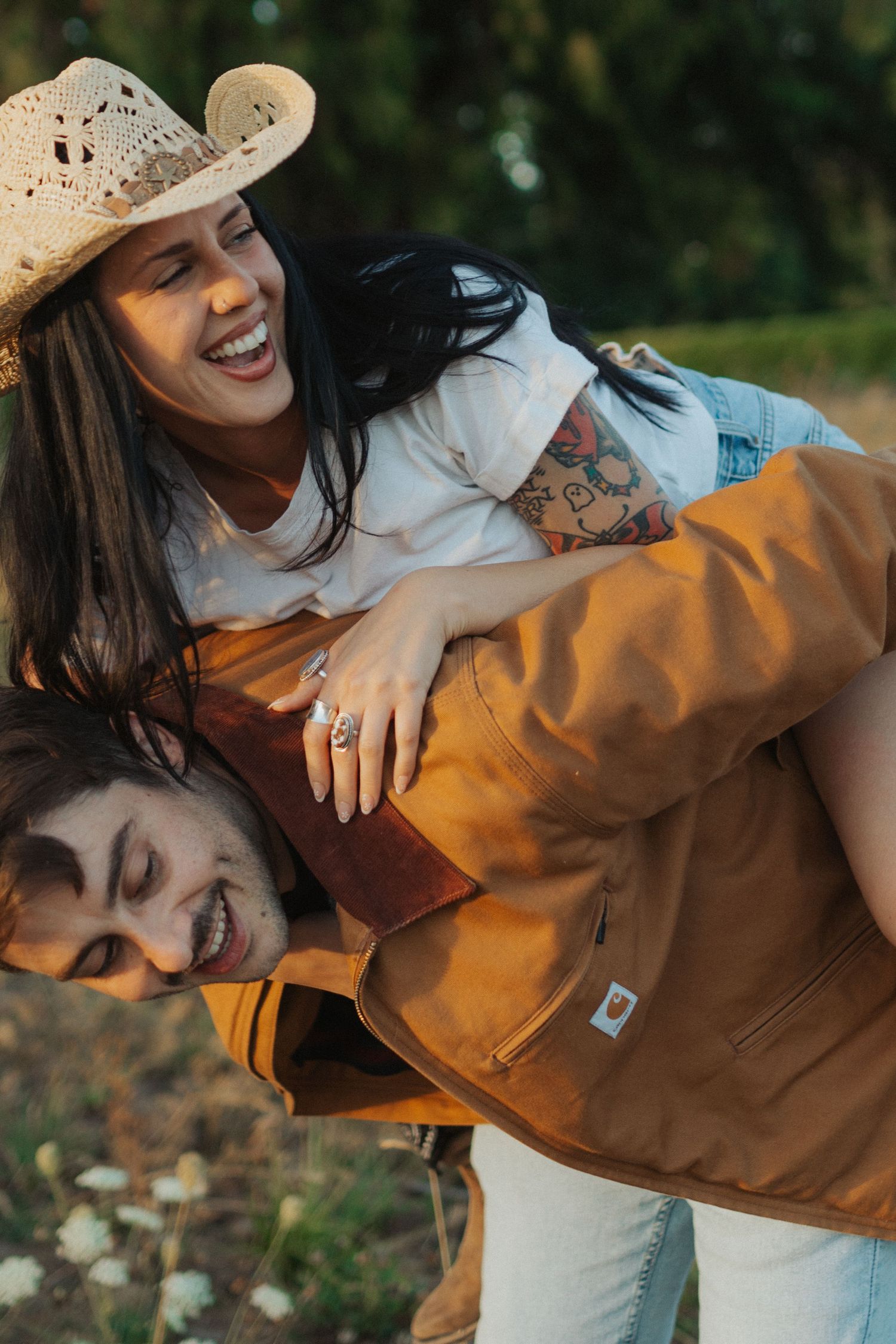A joyful couple laughs as the man gives the woman a piggyback ride in a sunny outdoor field.