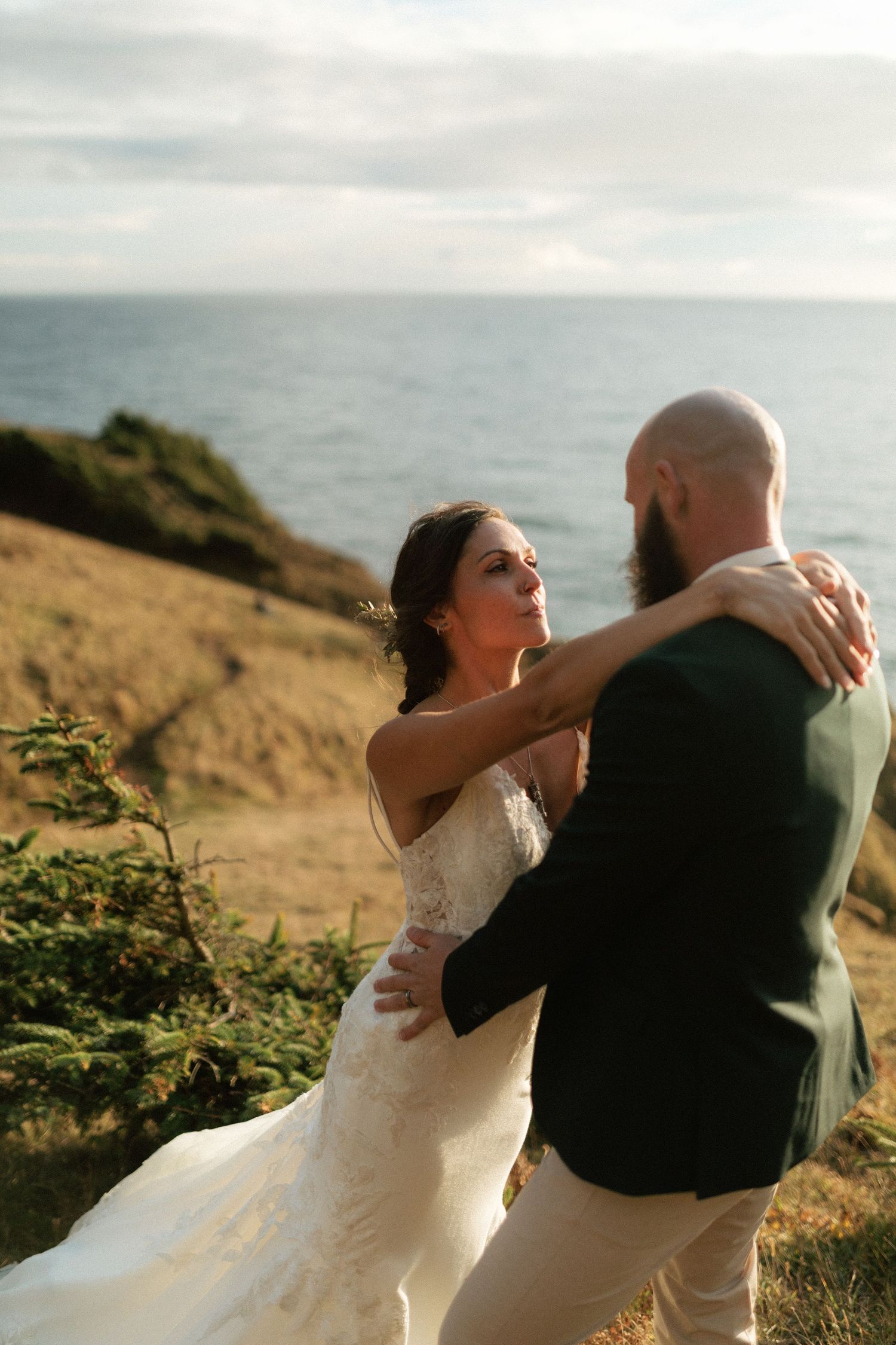 Bride and groom sharing a romantic dance on a cliffside with ocean views.