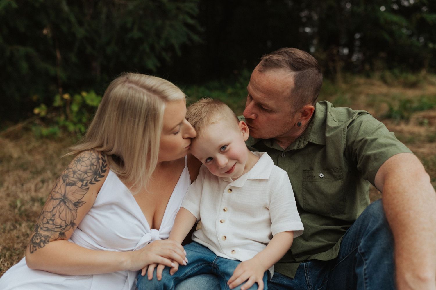 Loving parents kissing their young blond son on the cheeks during an outdoor family photo session.