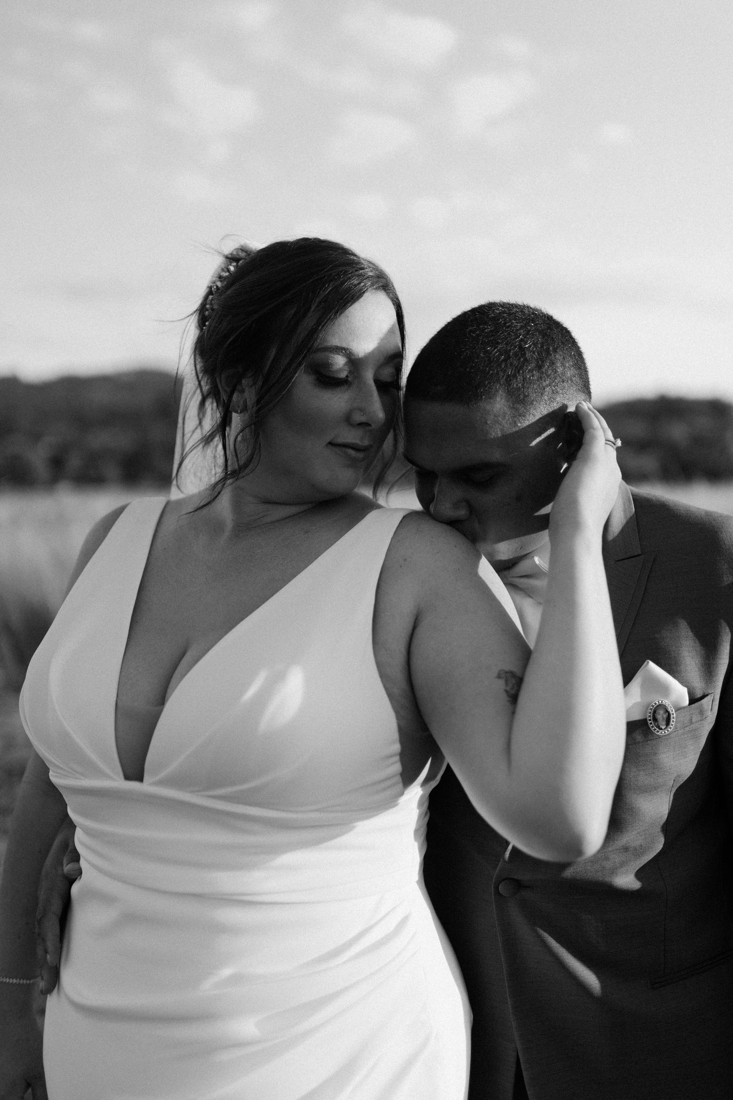 Black and white portrait of bride and groom in an intimate embrace in an open field at sunset.