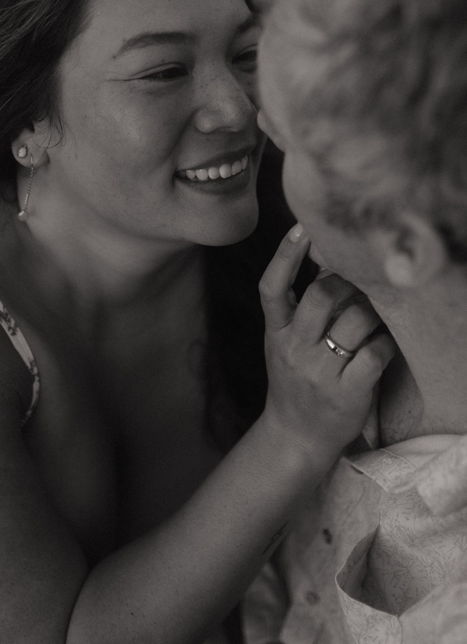 Black and white close-up of a smiling woman touching her partners face tenderly, wearing an engagement ring.