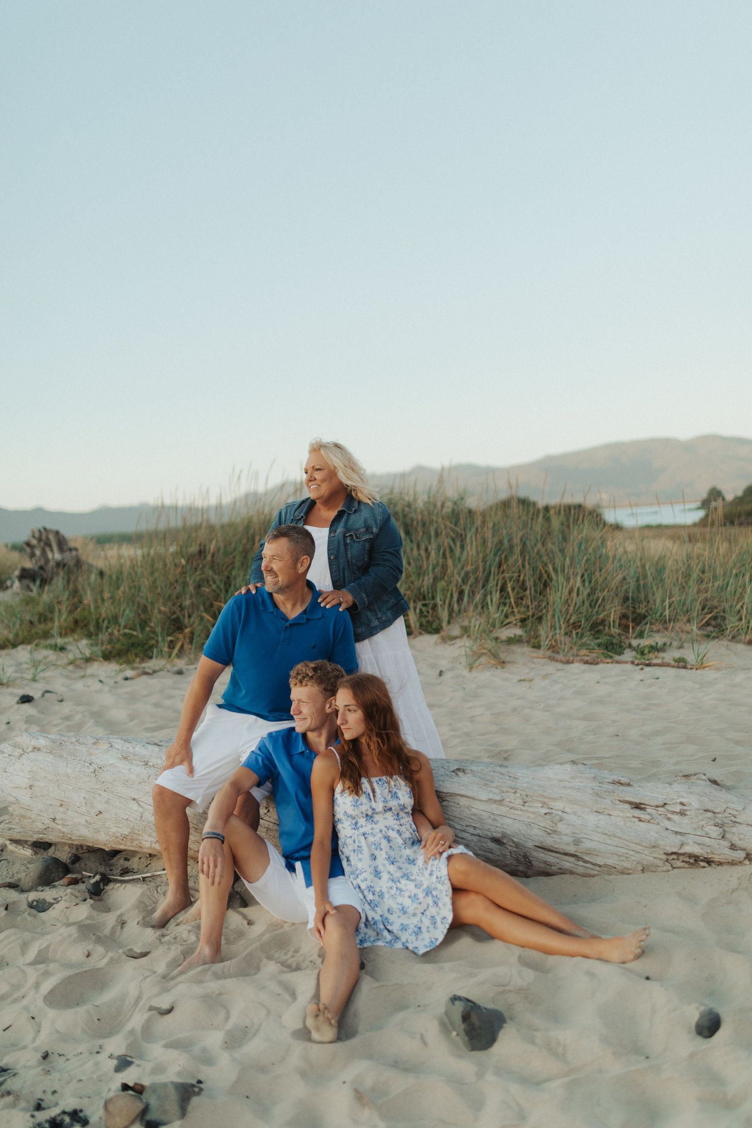 Family of four relaxing on sand dunes with tall grass and mountain views in background.
