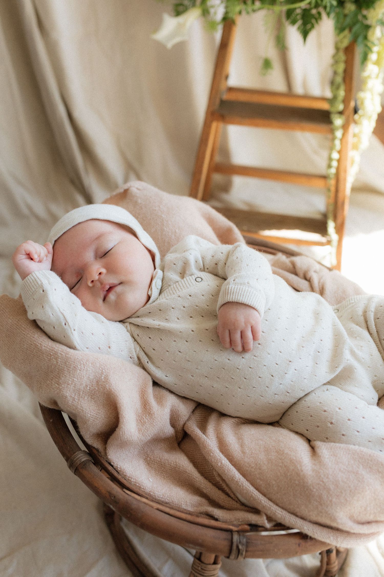 A peaceful newborn baby sleeps in a wicker basket wrapped in soft cream blankets.